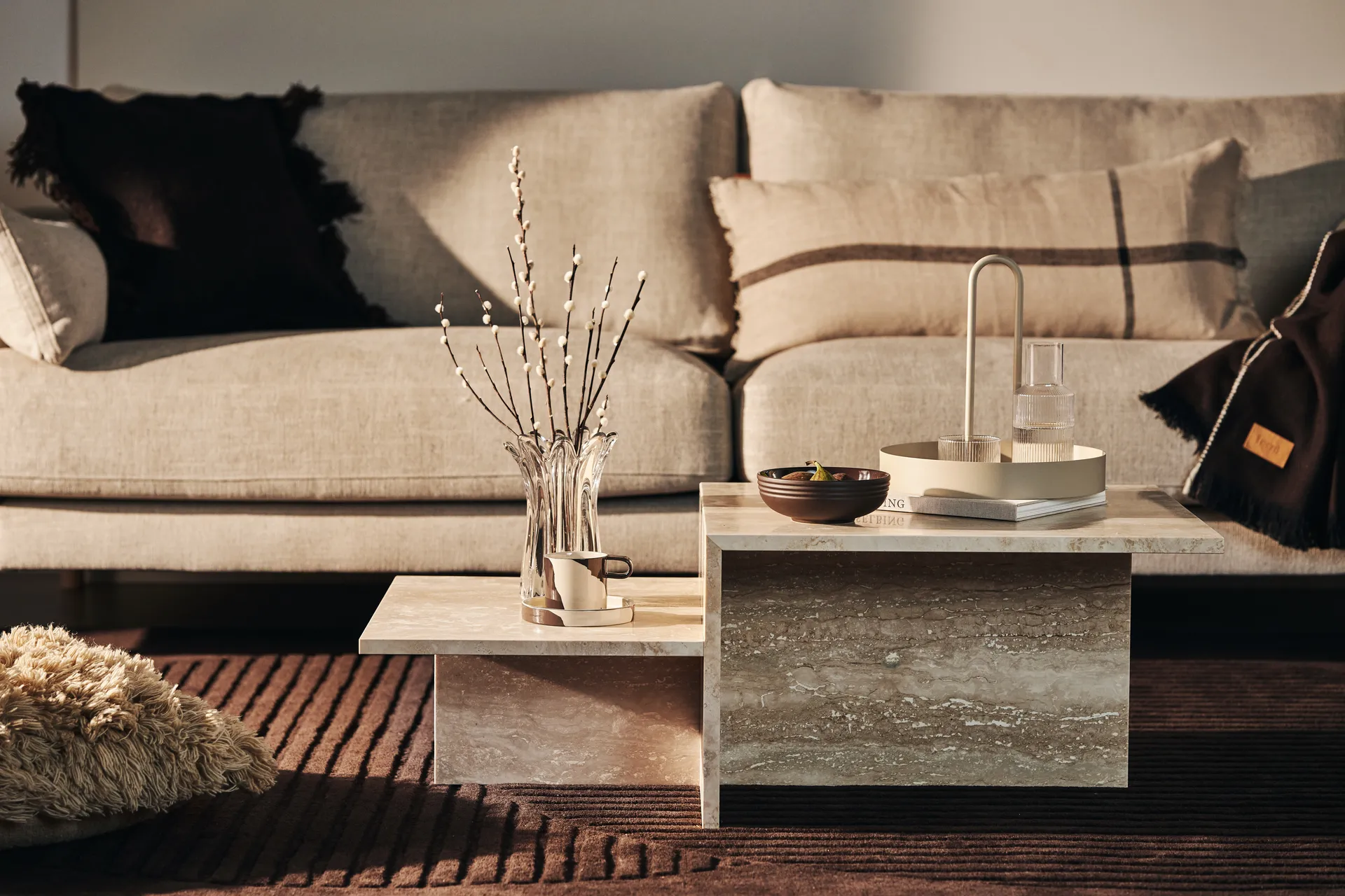 Trapsgewijze beige stenen salontafel voor een neutrale bank met decoratieve accessoires.