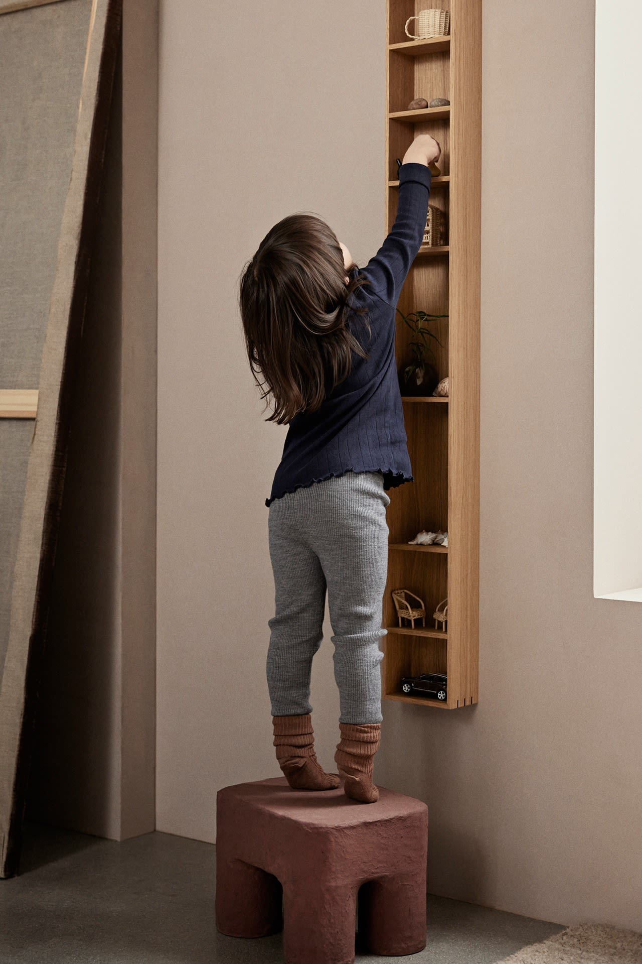 Een kind grijpt iets terwijl het op een donkerrood krukje van ferm LIVING staat - een heel praktisch idee voor de kinderkamer. 