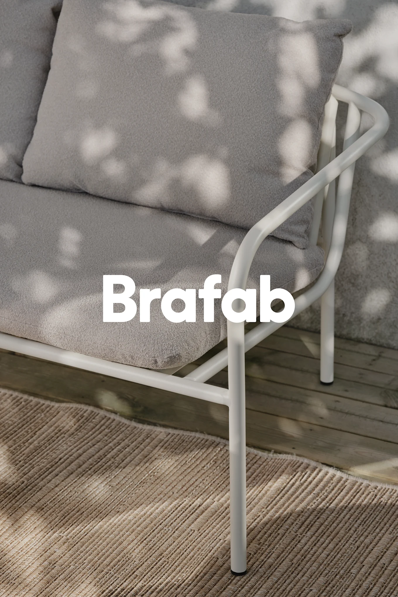 Brafab-logo over lichtgrijze buitenbank, wit metalen frame, op beige vloerkleed op houten vlonder met schaduwen.