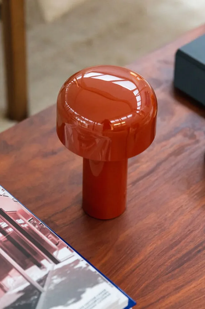 Glanzende oranje paddenstoellamp op een houten tafel, met een tijdschrift op de voorgrond.
