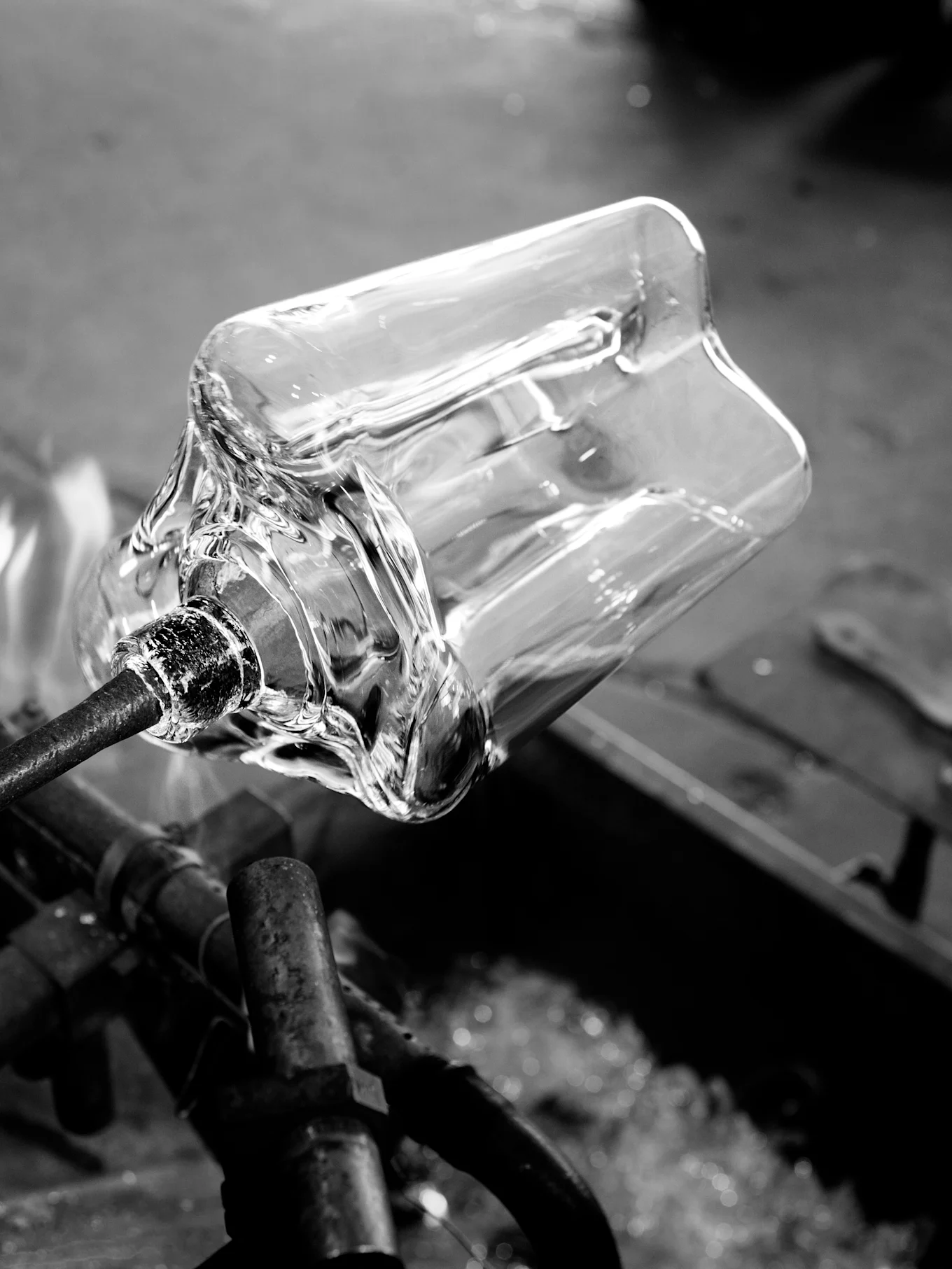 Doorzichtig glazen vat wordt gevormd op een metalen staaf met hitte, zwart-wit.