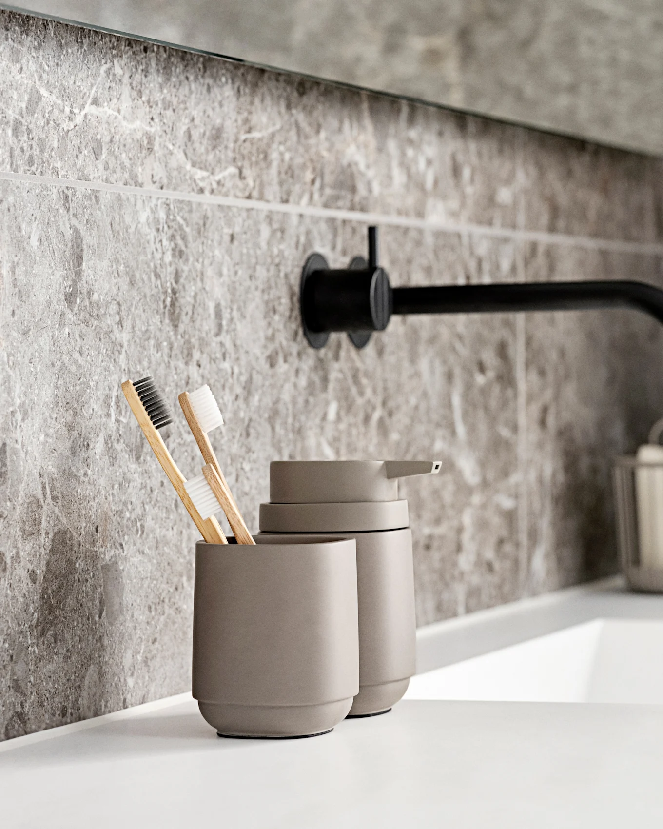 Moderne badkamer met witte wastafel, zwarte wandkraan, grijze marmerlook tegels en milieuvriendelijke tandenborstels.