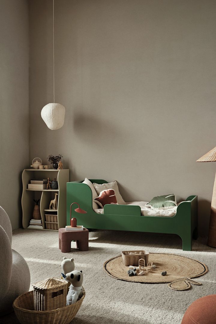 Hier zie je een kinderkamer met neutraal gekleurde muren en een groen bed. Gekleurde meubels zijn een goede manier om kleur te brengen in een kinderkamer. 