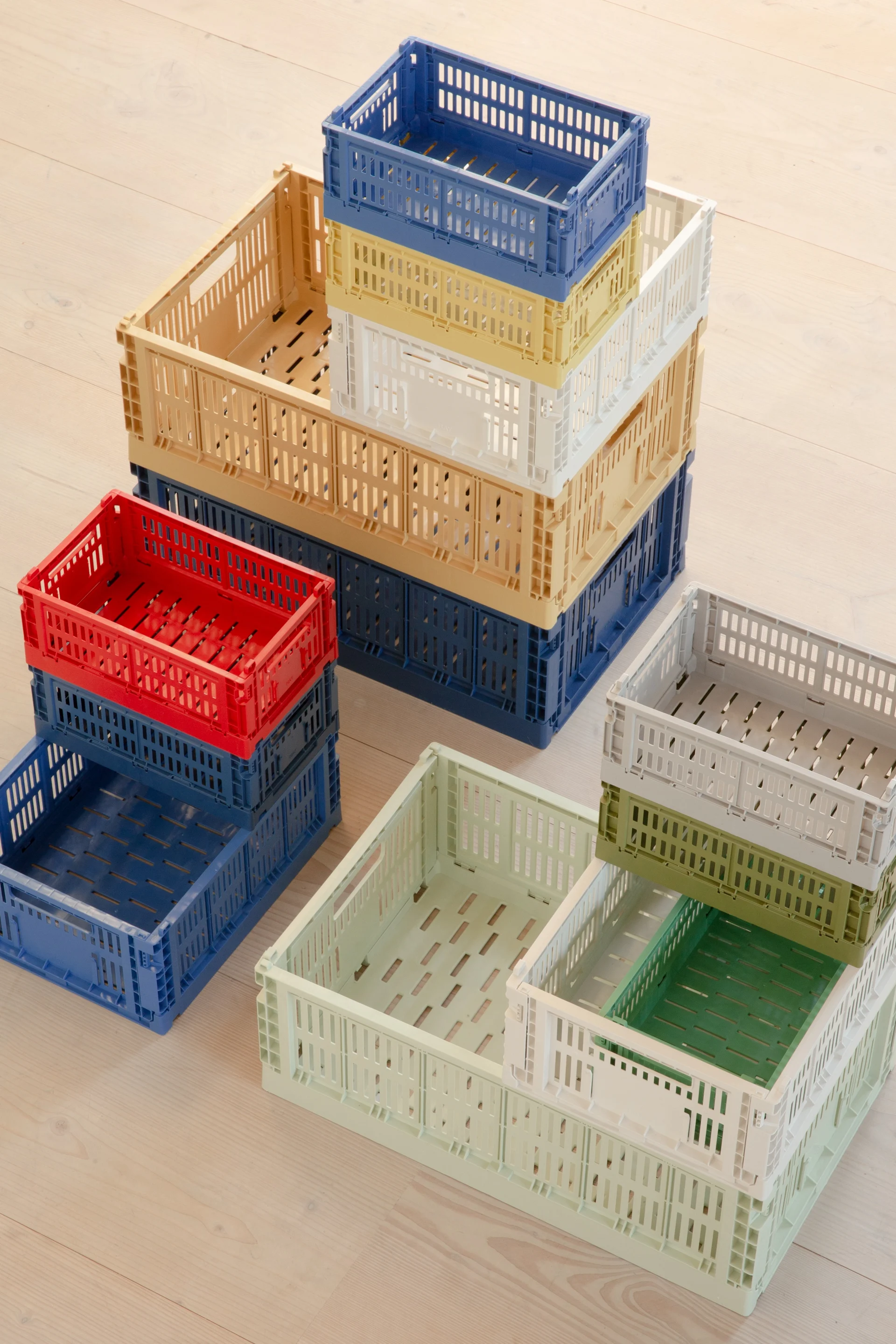 Stapels kleurrijke, geperforeerde plastic vouwkratten op een lichte houten vloer.