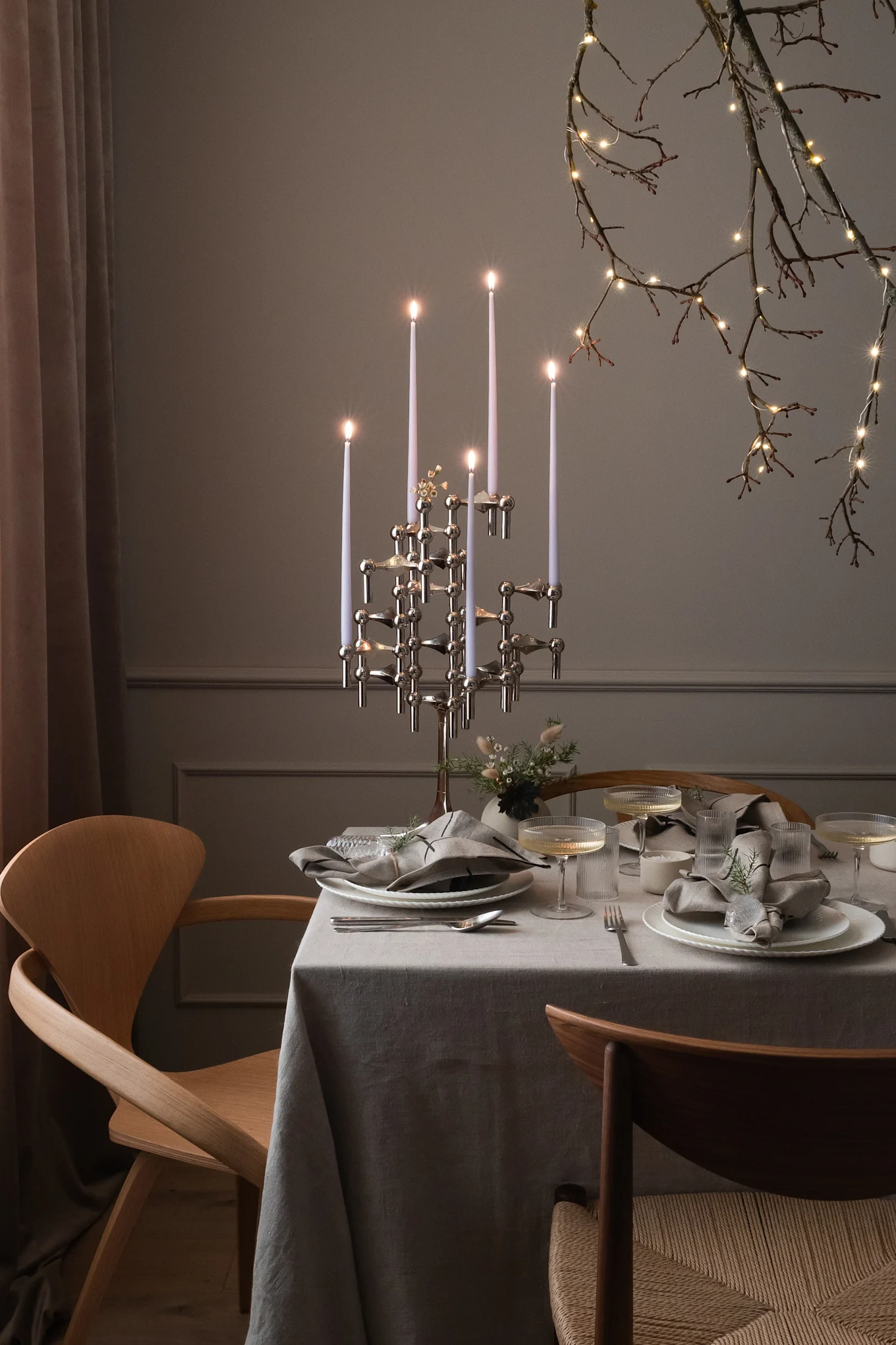 Een eettafel gedekt voor een speciale gelegenheid met een moderne kandelaar, couverts en verlichte takken.