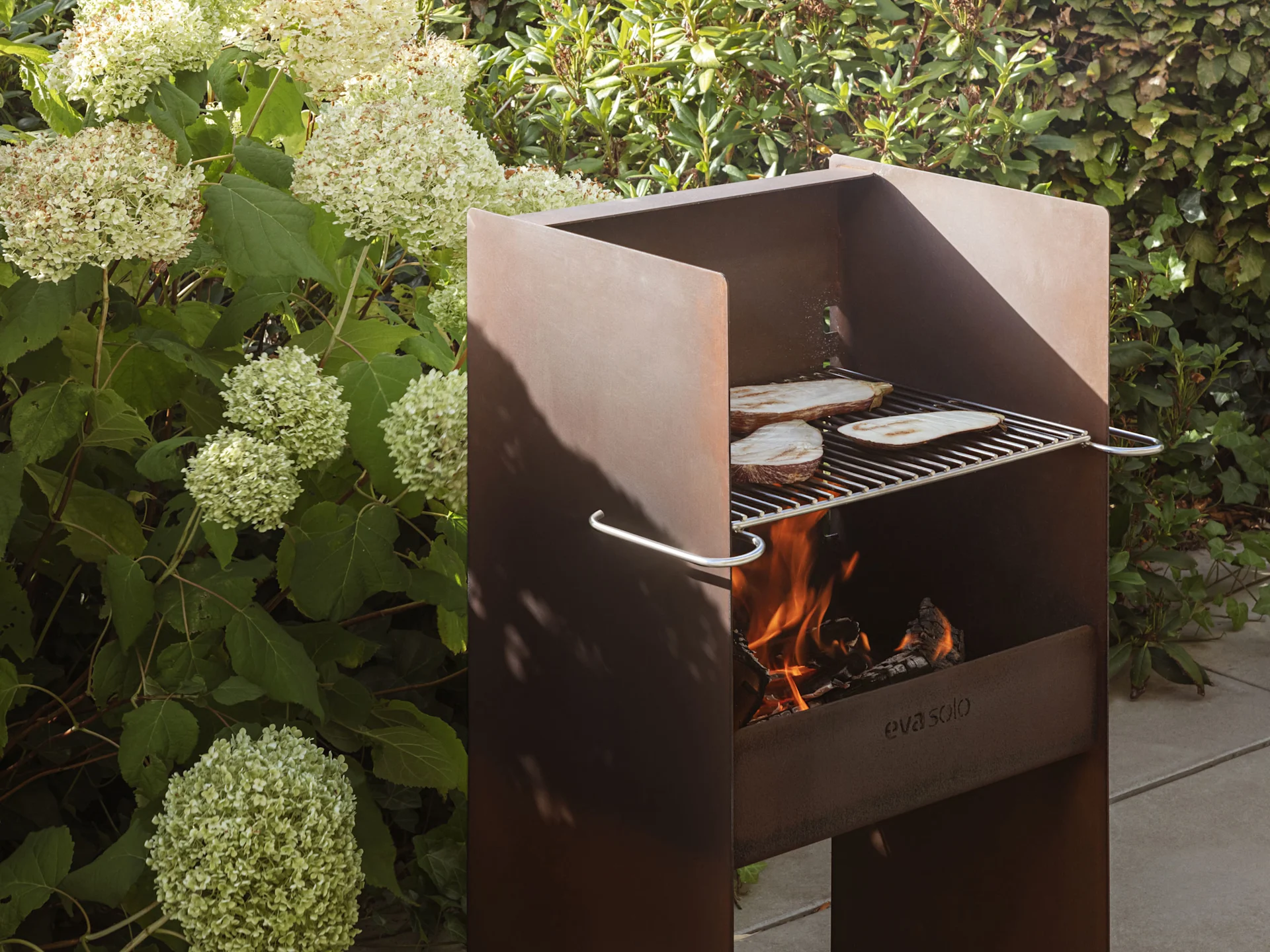 Een rustieke metalen buitenbarbecue met vlammen en aubergineplakken die op het rooster garen.