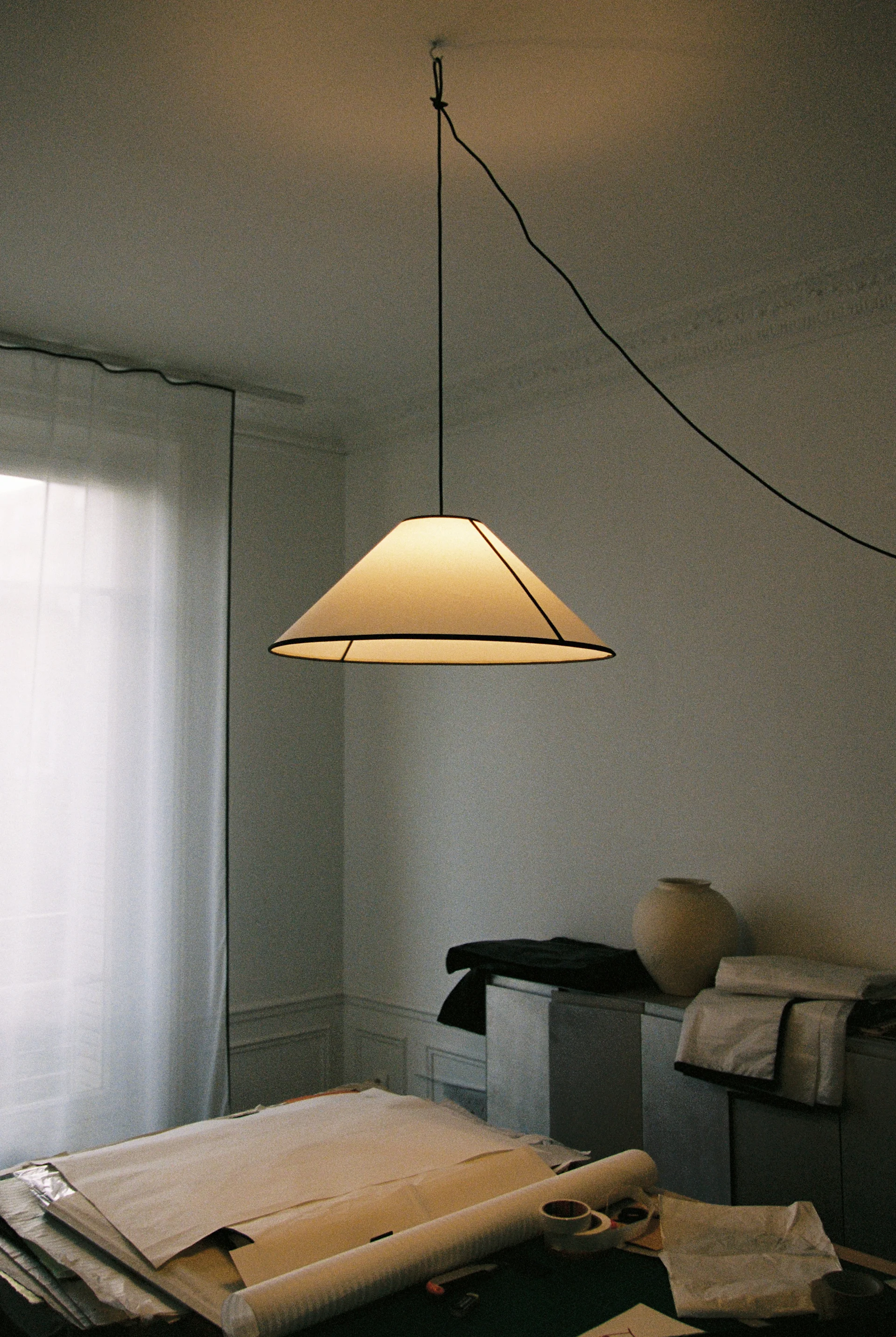 Een gezellige kamer met een crèmekleurige pluizige fauteuil, een beige verstelbare vloerlamp en een donkerhouten plank met kunst en boeken.