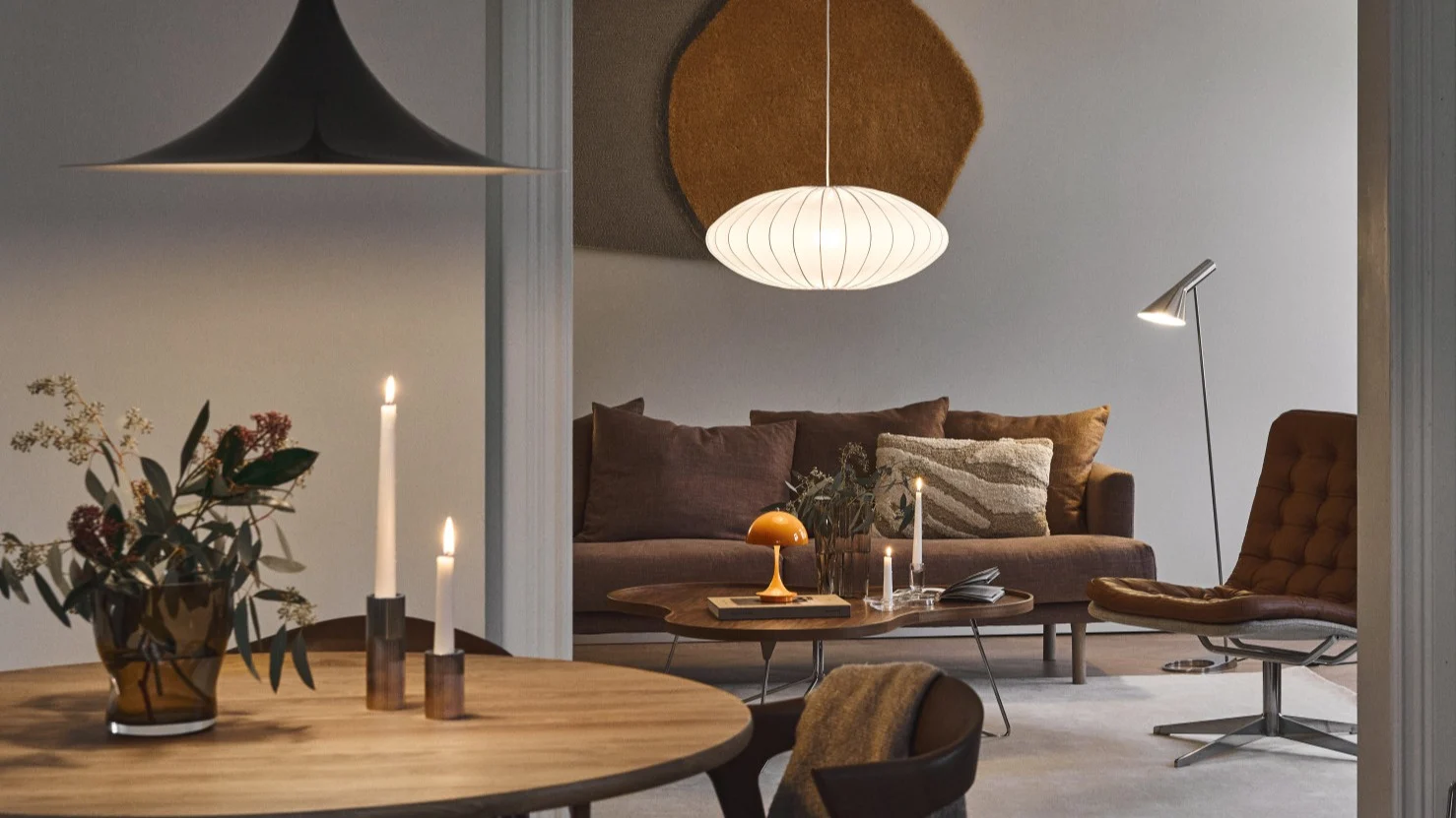 Warm verlichte moderne eet- en woonkamer met designlampen, bruine bank en lederen loungefauteuil.