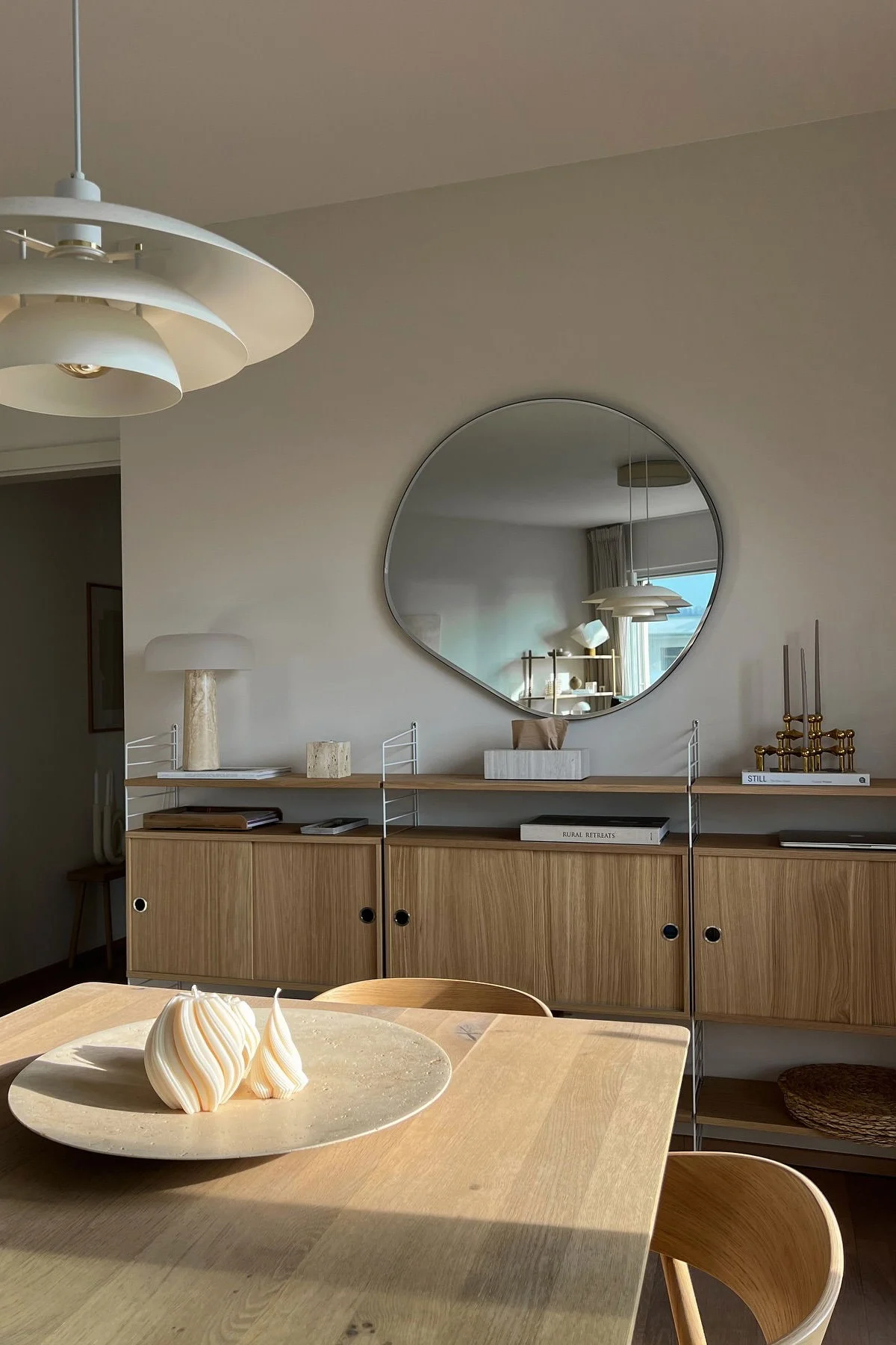 Moderne eetkamer met houten tafel, twee spiraalkaarsen, plank, onregelmatige spiegel en gelaagde lamp.