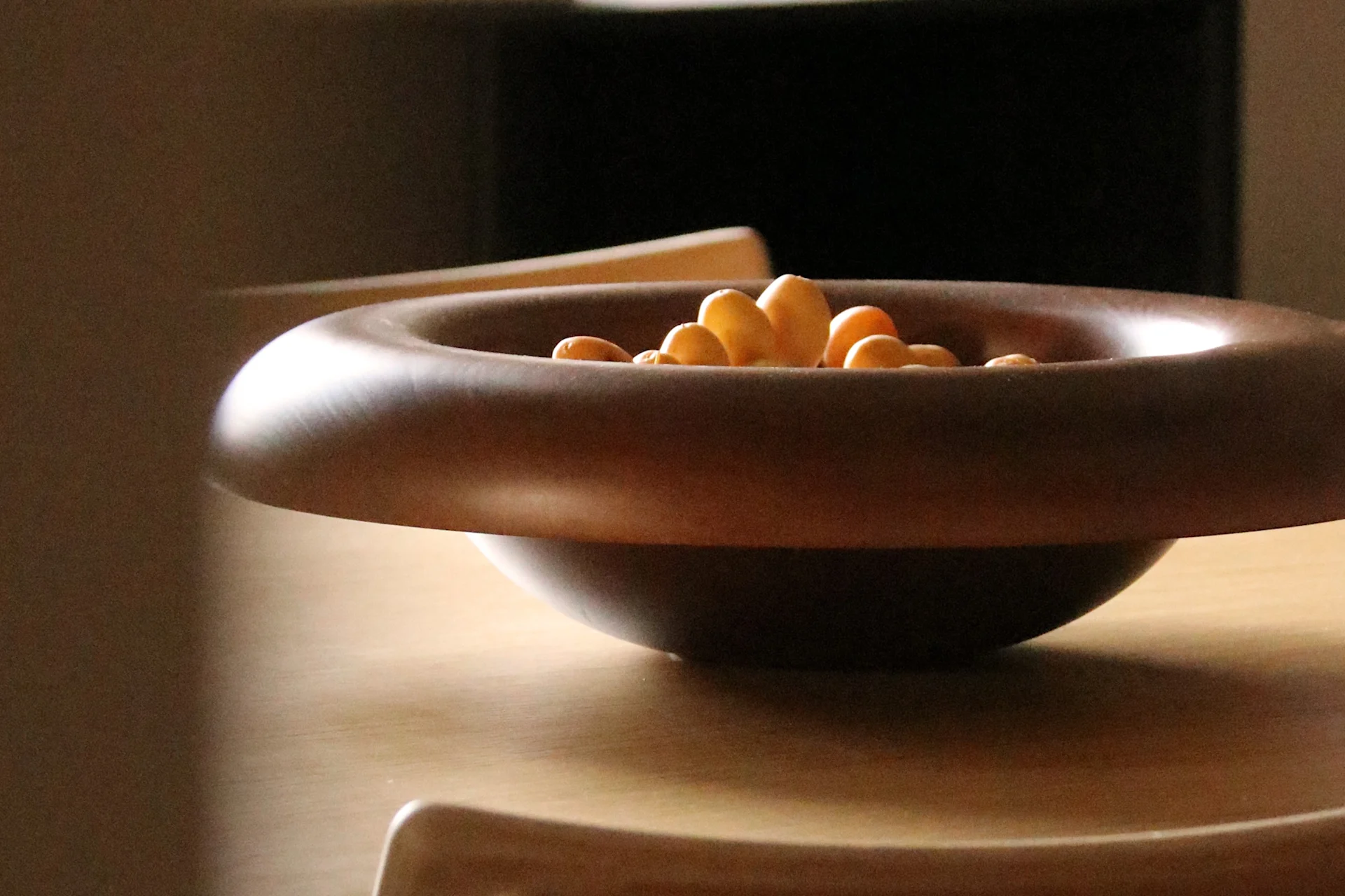 Donkerbruine houten kom met brede rand gevuld met lichtgekleurde snacks op een lichte houten tafel.