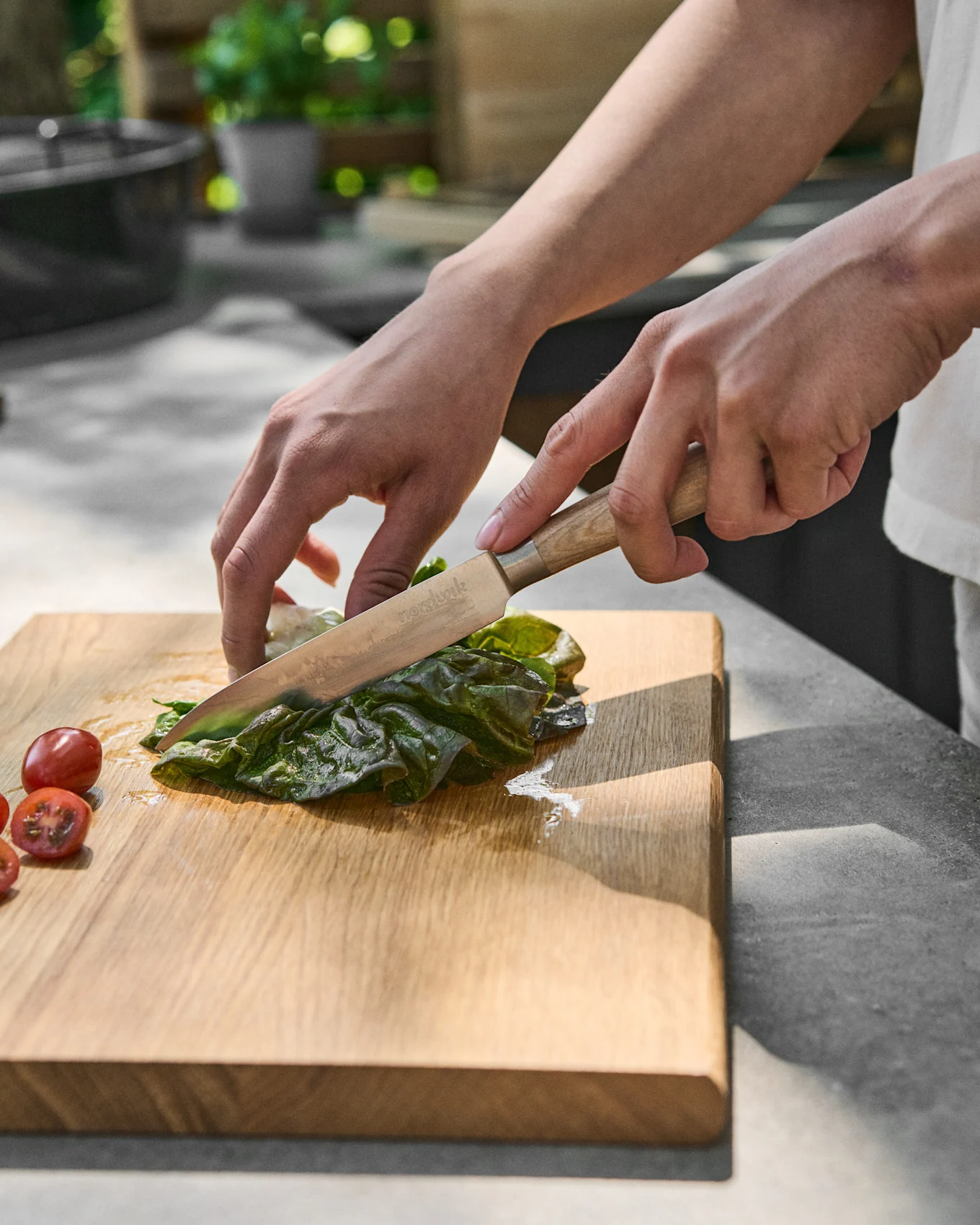 Handen snijden groene sla op een houten snijplank naast cherrytomaten.