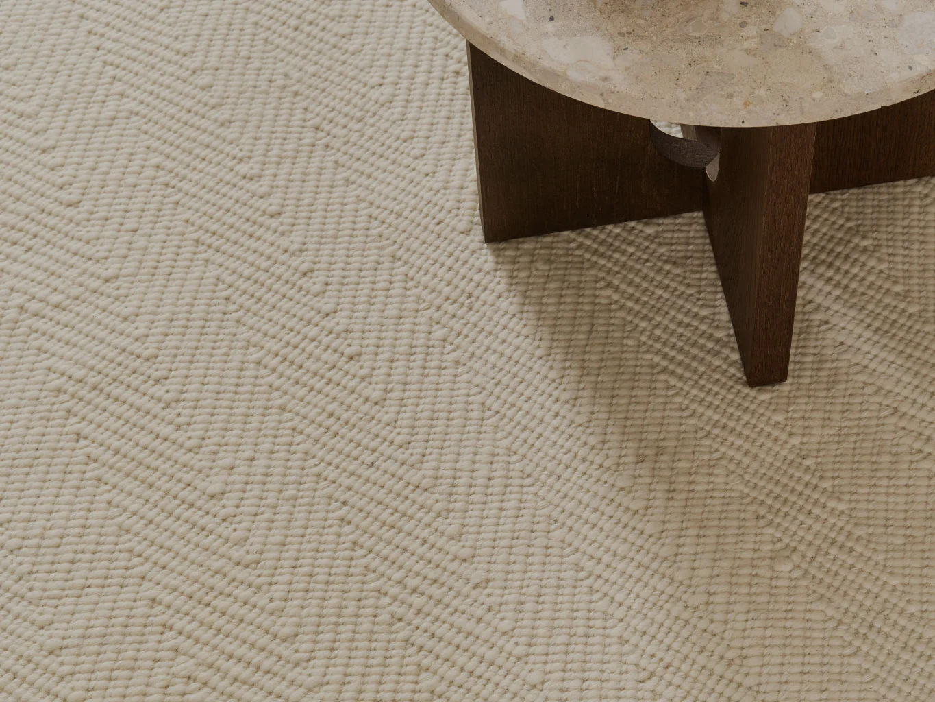 Close-up van een crèmekleurig getextureerd vloerkleed met een chevronpatroon, naast een tafel met een stenen blad.