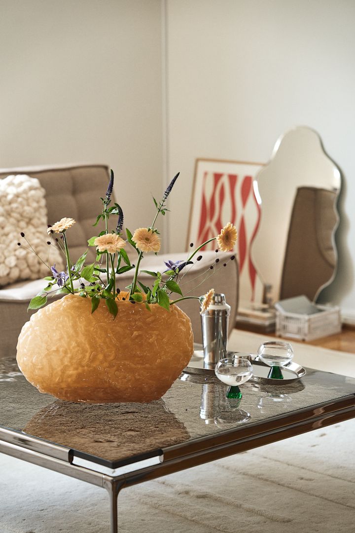 Een van de statementstukken van Byon is de Corallo-vaas, gemaakt van mondgeblazen glas met een zware, solide structuur, hier in geel op een salontafel met een rookglas tafelblad.