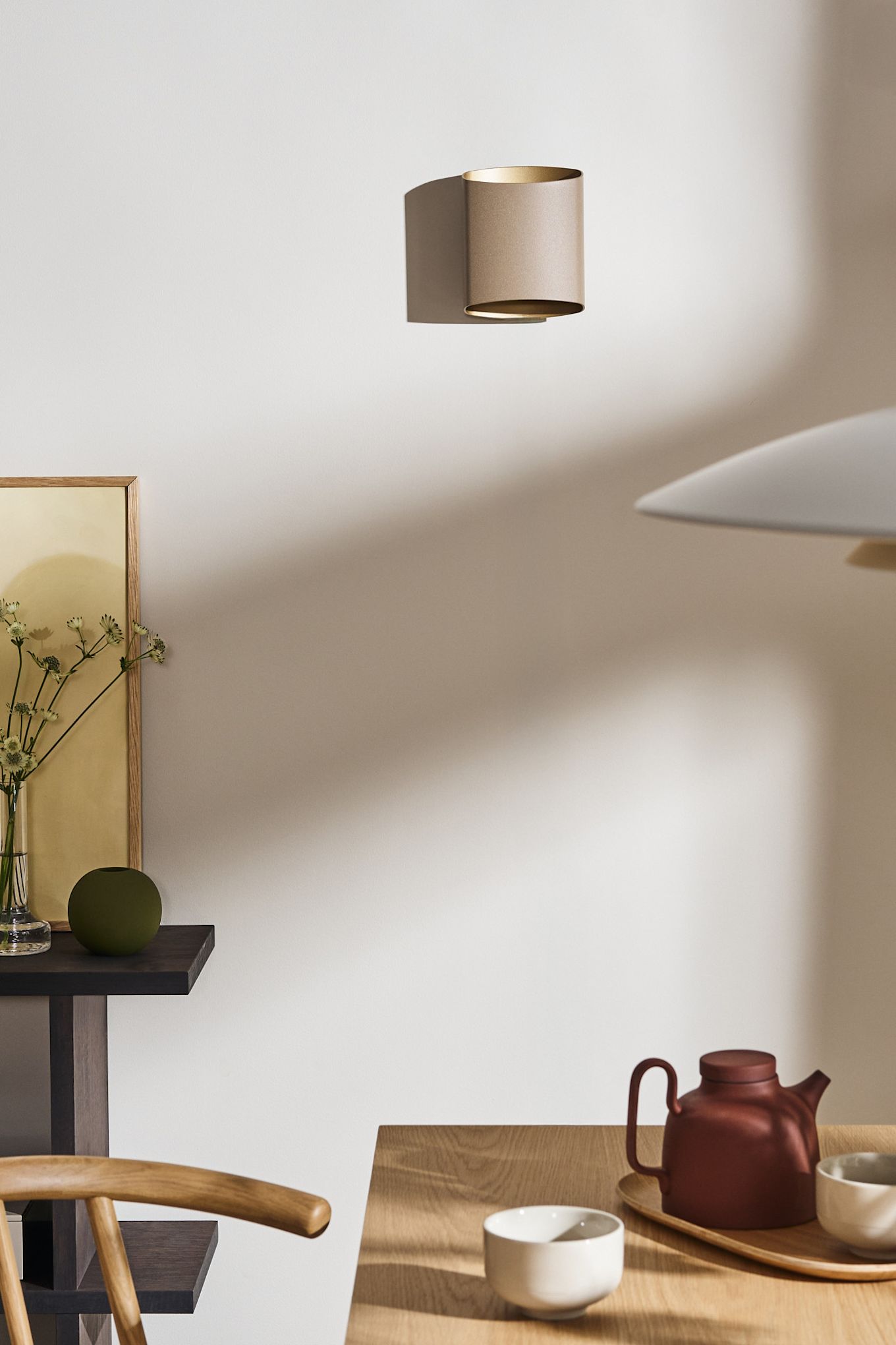 Breng lagen aan in de verlichting voor de eetkamer, bijvoorbeeld met de Sinne wandlamp van Belid, hier getoond in beige op de muur van een eetkamer.