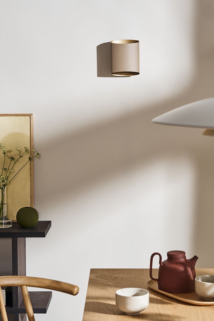 Breng lagen aan in de verlichting voor de eetkamer, bijvoorbeeld met de Sinne wandlamp van Belid, hier getoond in beige op de muur van een eetkamer.