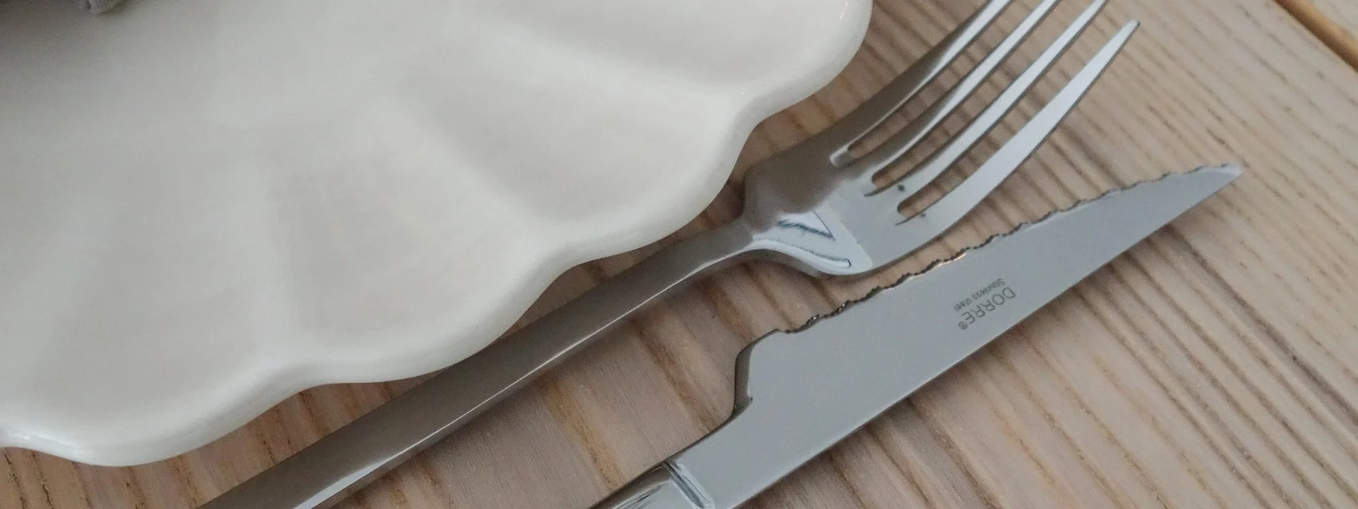 Elegante tafelsetting met wit gegolfd bord, grijze linnen servet, gouden servetring, zilveren vork en mes, en wijnglas op houten tafel.