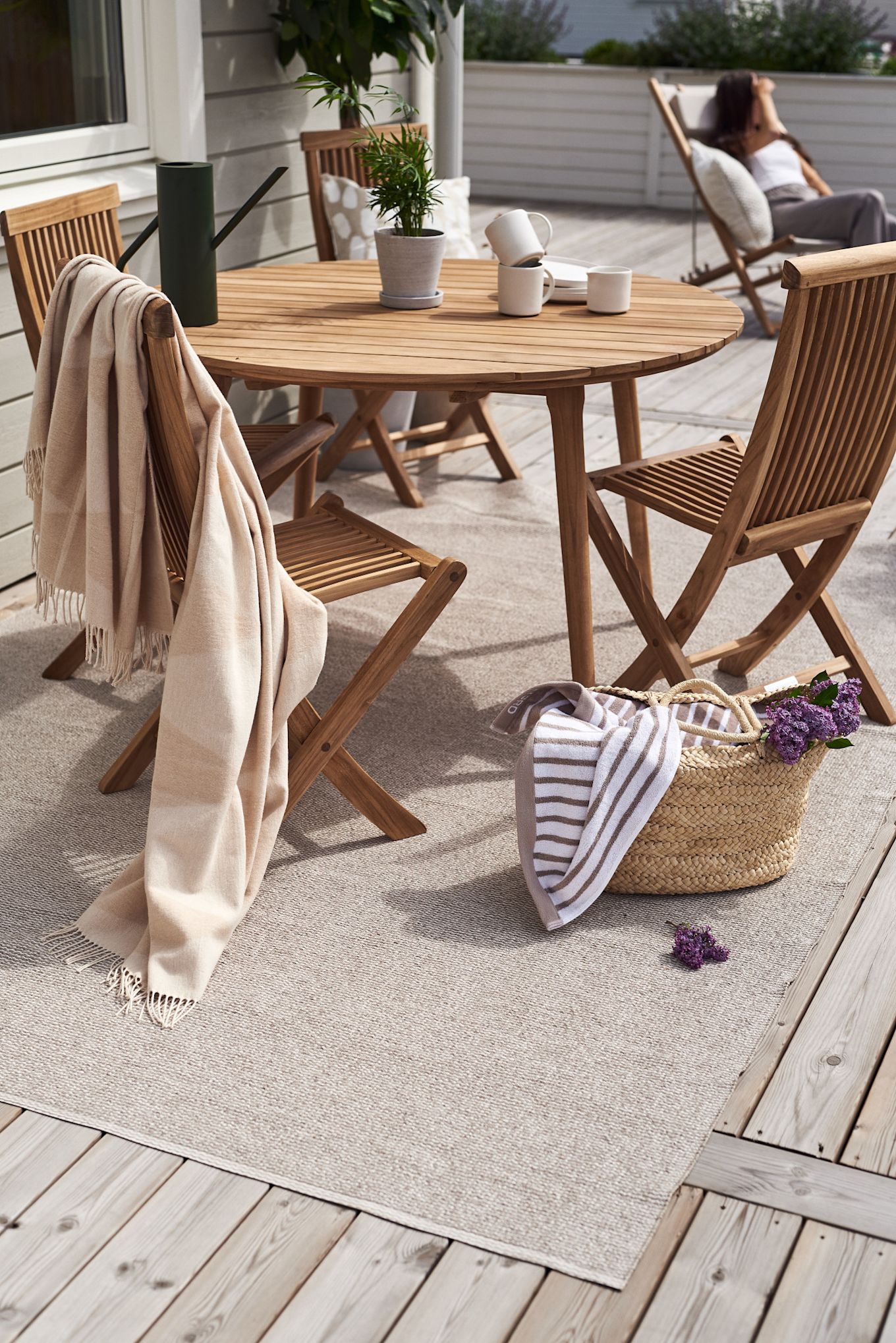Een terras met houten meubels, bijvoorbeeld de Aneboda balkonset uit 1898 en het Rime katoenen vloerkleed van Scandi Living op het Mellow plastic tapijt.