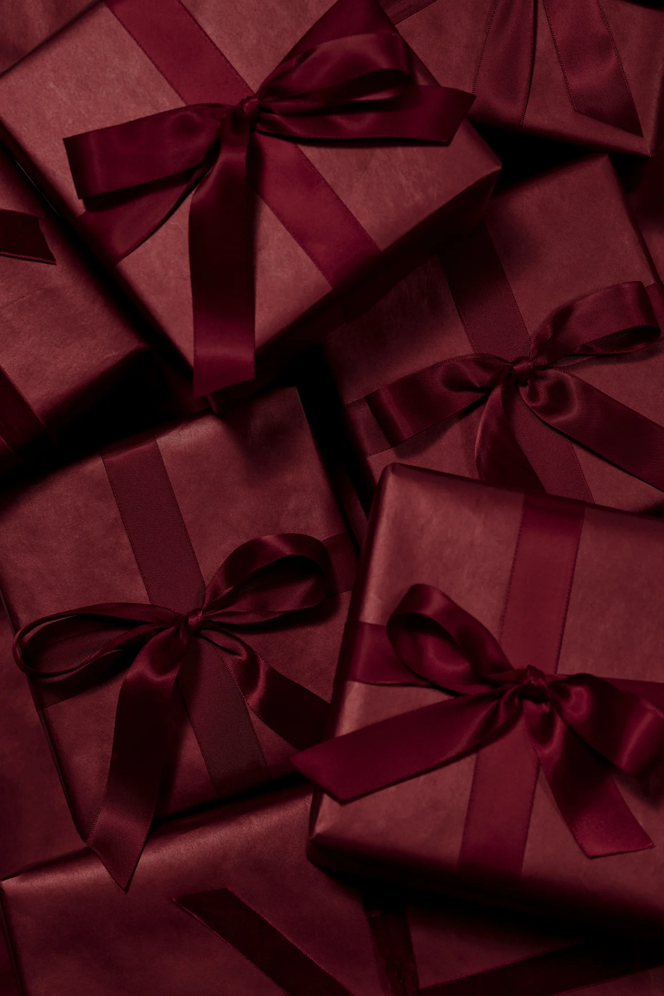 Meerdere donkerrode cadeauverpakkingen met bijpassende satijnen linten en strikken.