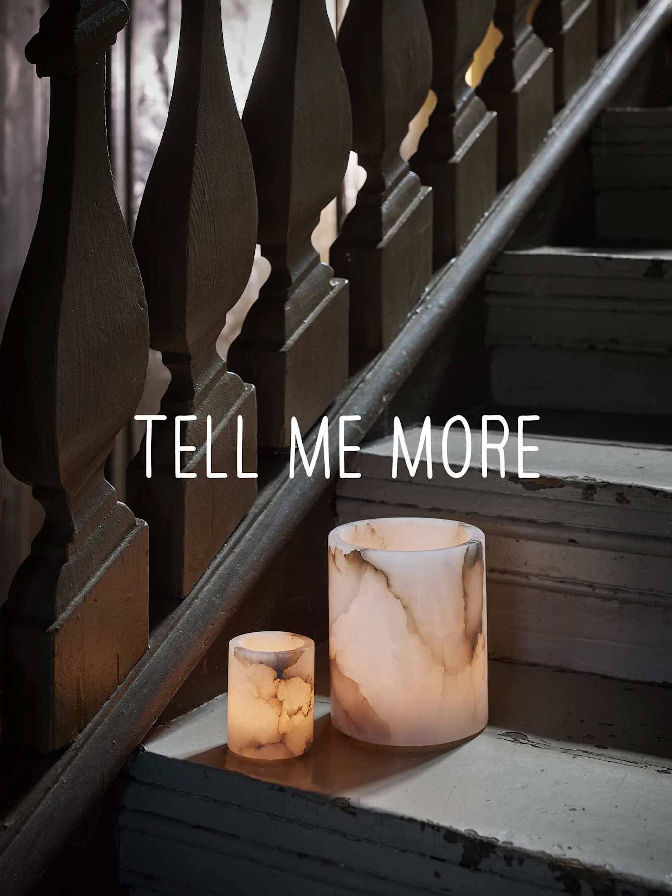 Twee gloeiende onyx-achtige kandelaars op een versleten houten trap, met de tekst "TELL ME MORE".