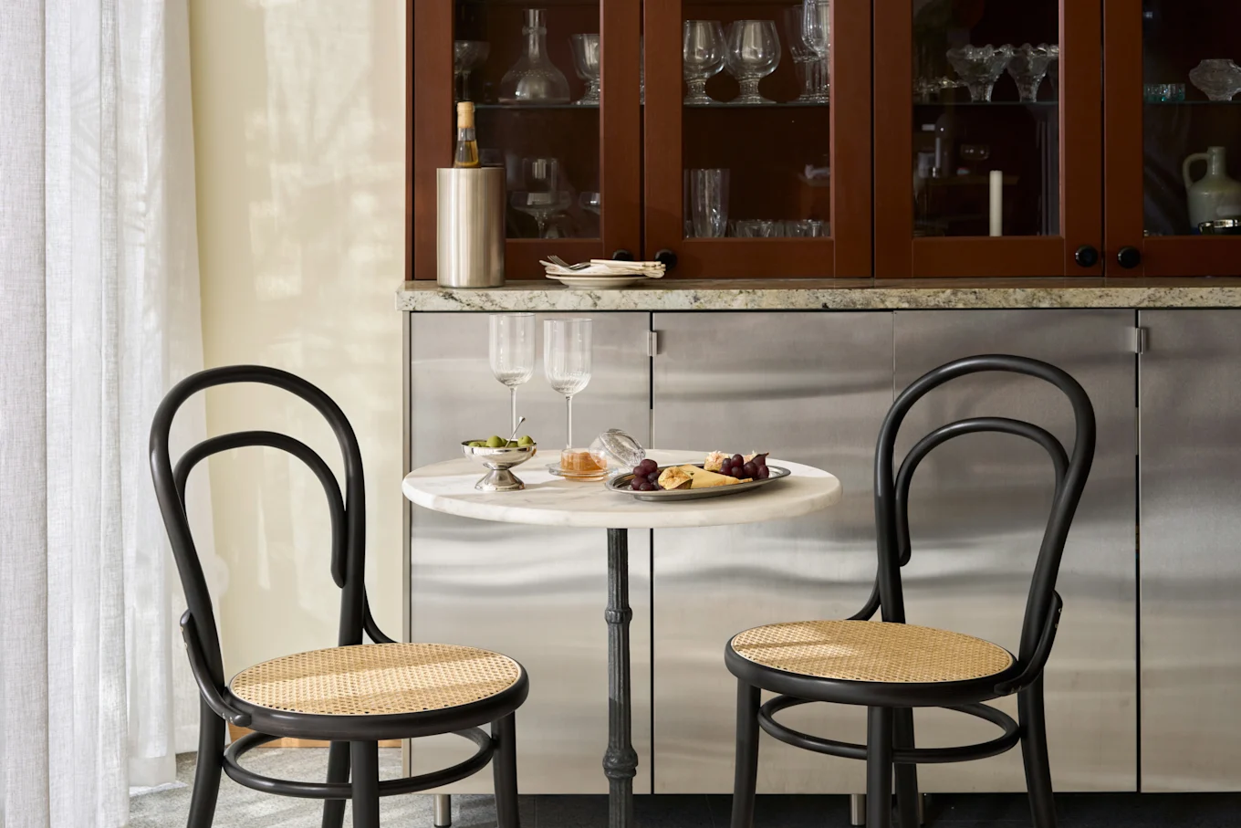 Gezellige eethoek met marmeren tafel, twee zwarte stoelen, schaal met kaas, fruit, olijven en wijnglazen.