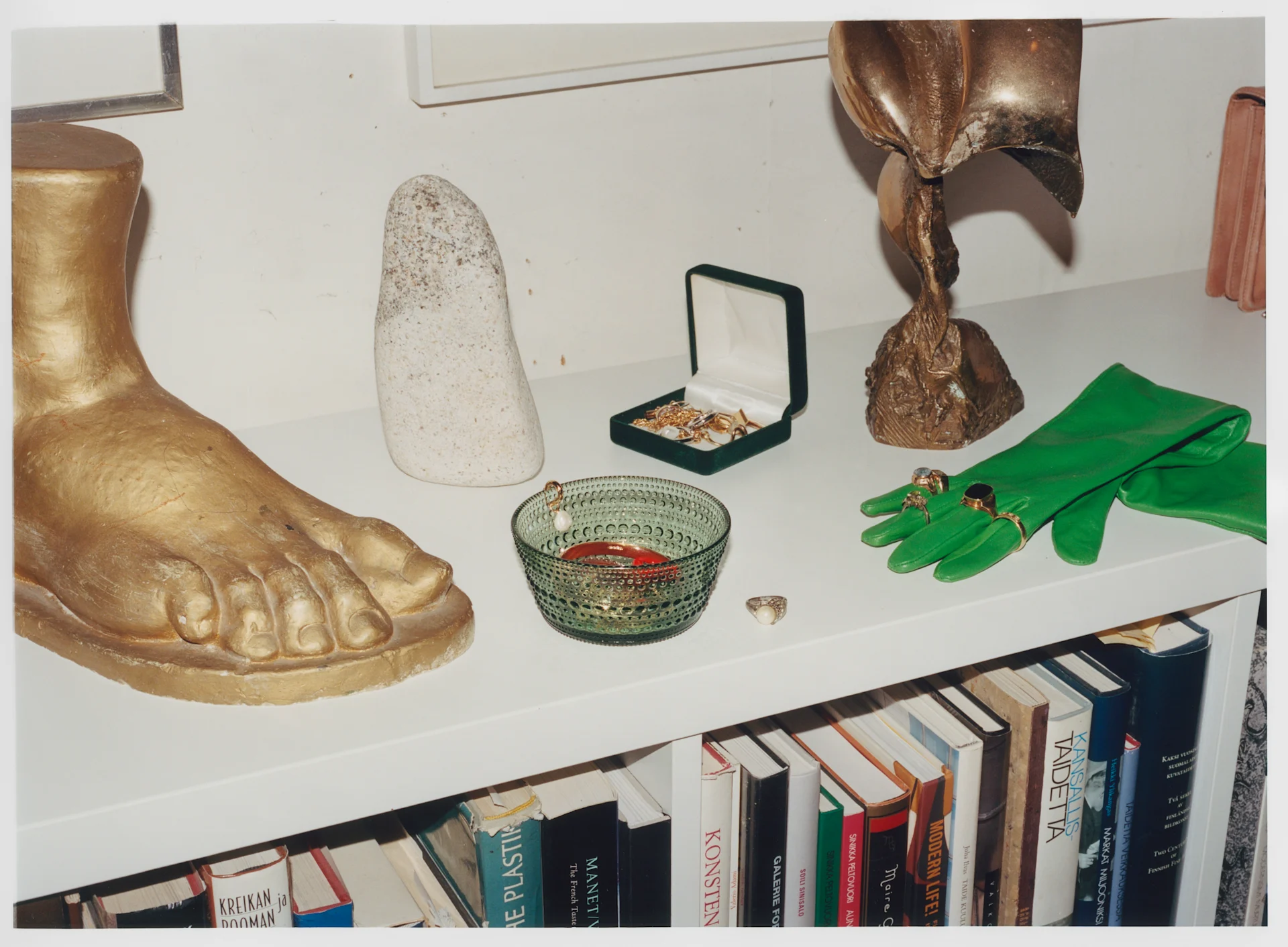 Iittala gaat een nieuw tijdperk in maar de producten zijn hetzelfde, hier Kastehelmi-kom in groen op een dressoir met beelden en handschoenen.