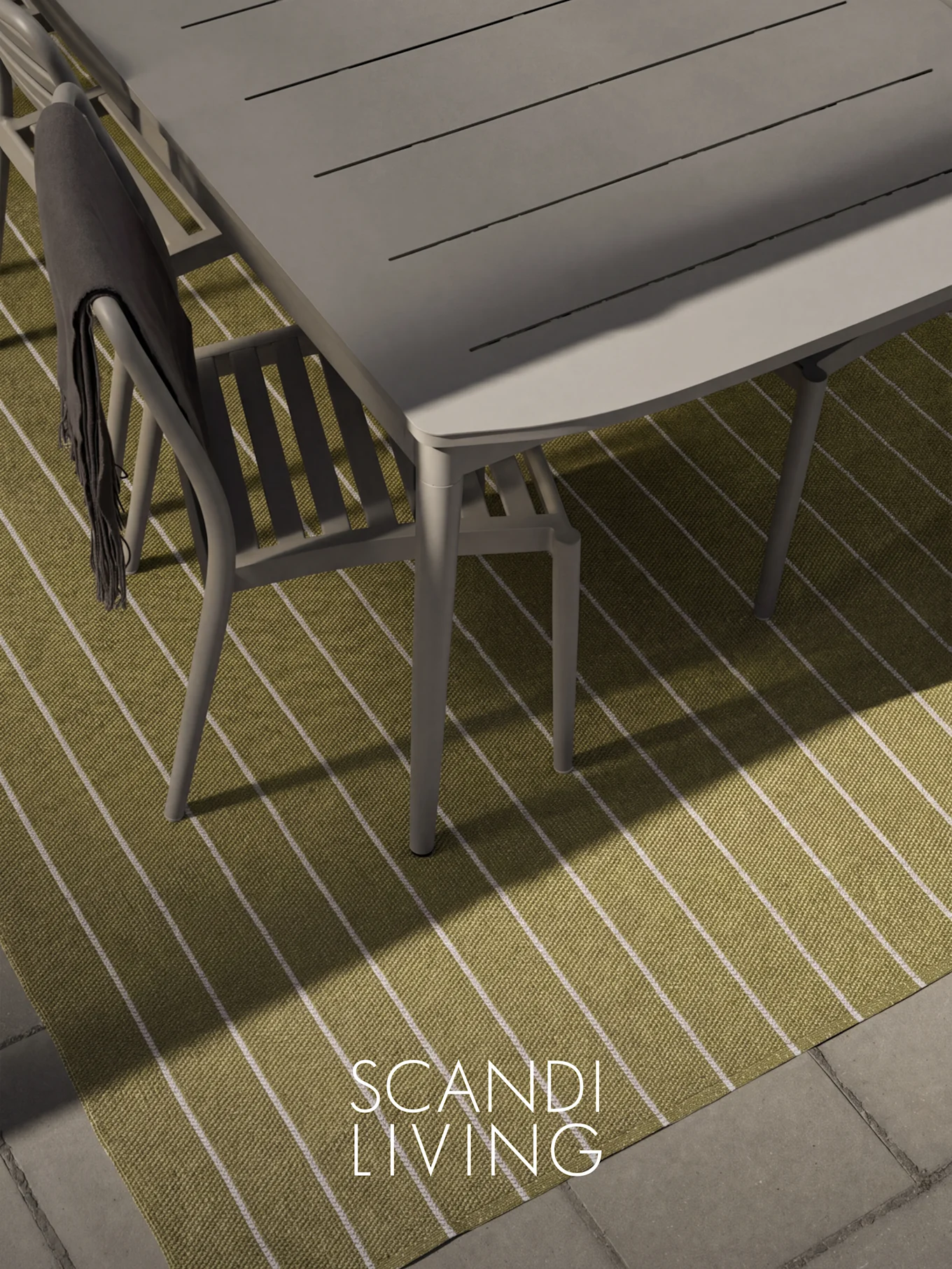 Bovenaanzicht van een grijze buiteneettafel en stoel met een donkere plaid op een groen-wit gestreept tapijt.