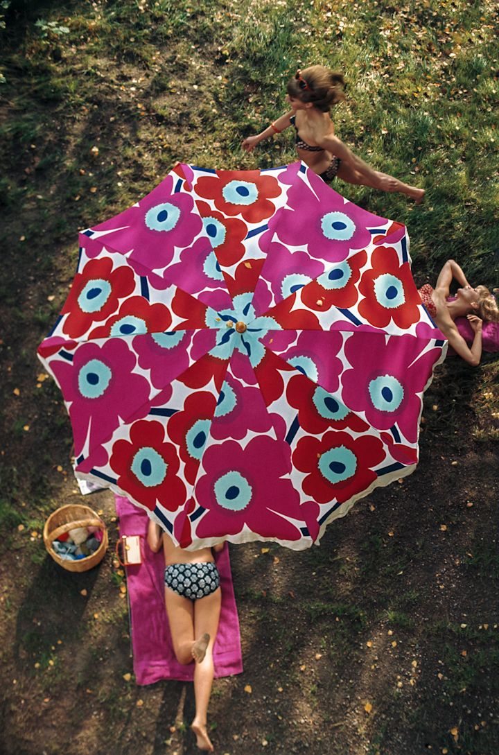 Een afbeelding van een Unikko parasol van bovenaf met een vrouw in de zon eronder.