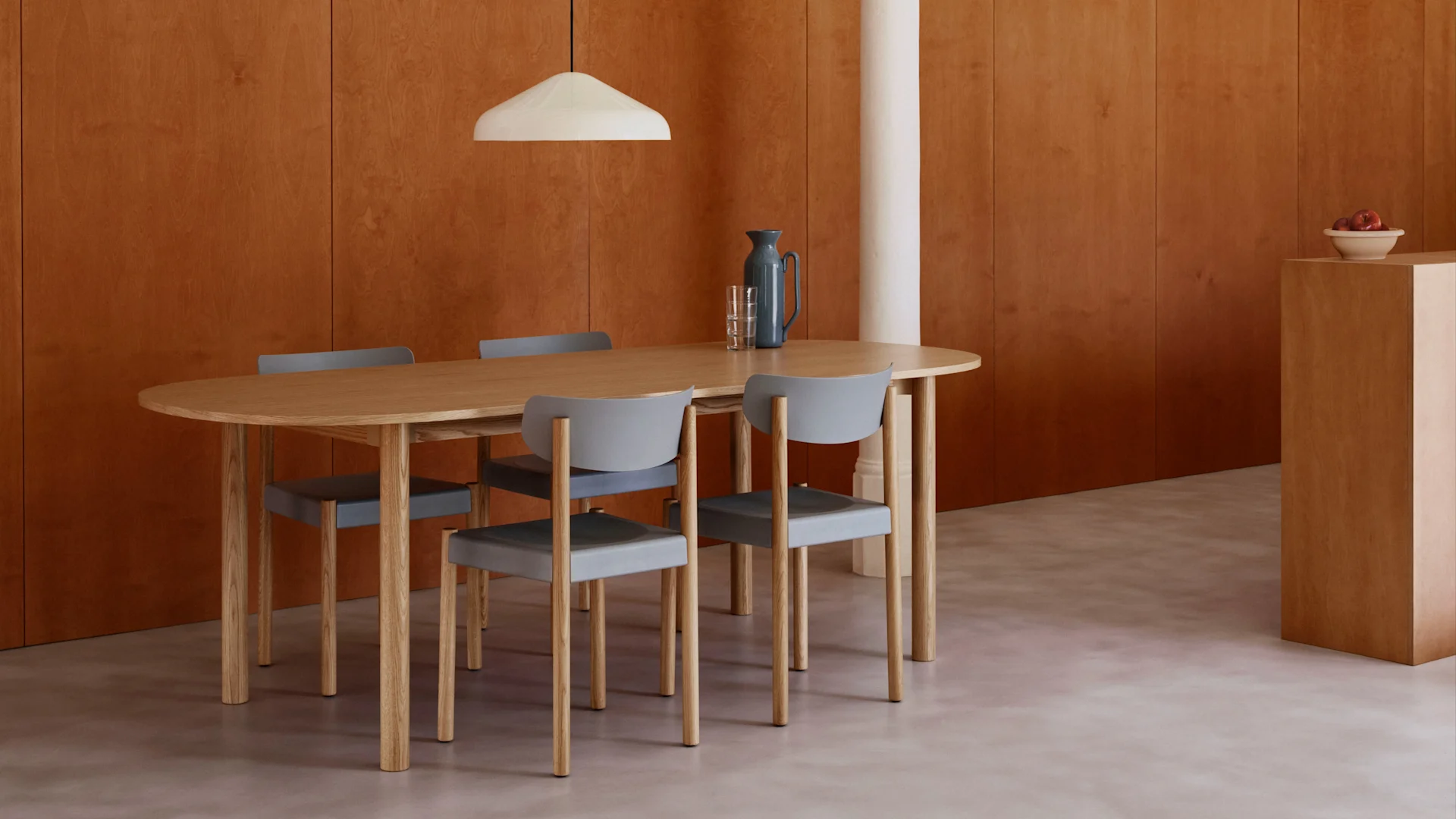 Moderne eetkamer met ovale houten tafel, vier grijze stoelen, warme houten lambrisering, lichte vloer en een witte hanglamp.