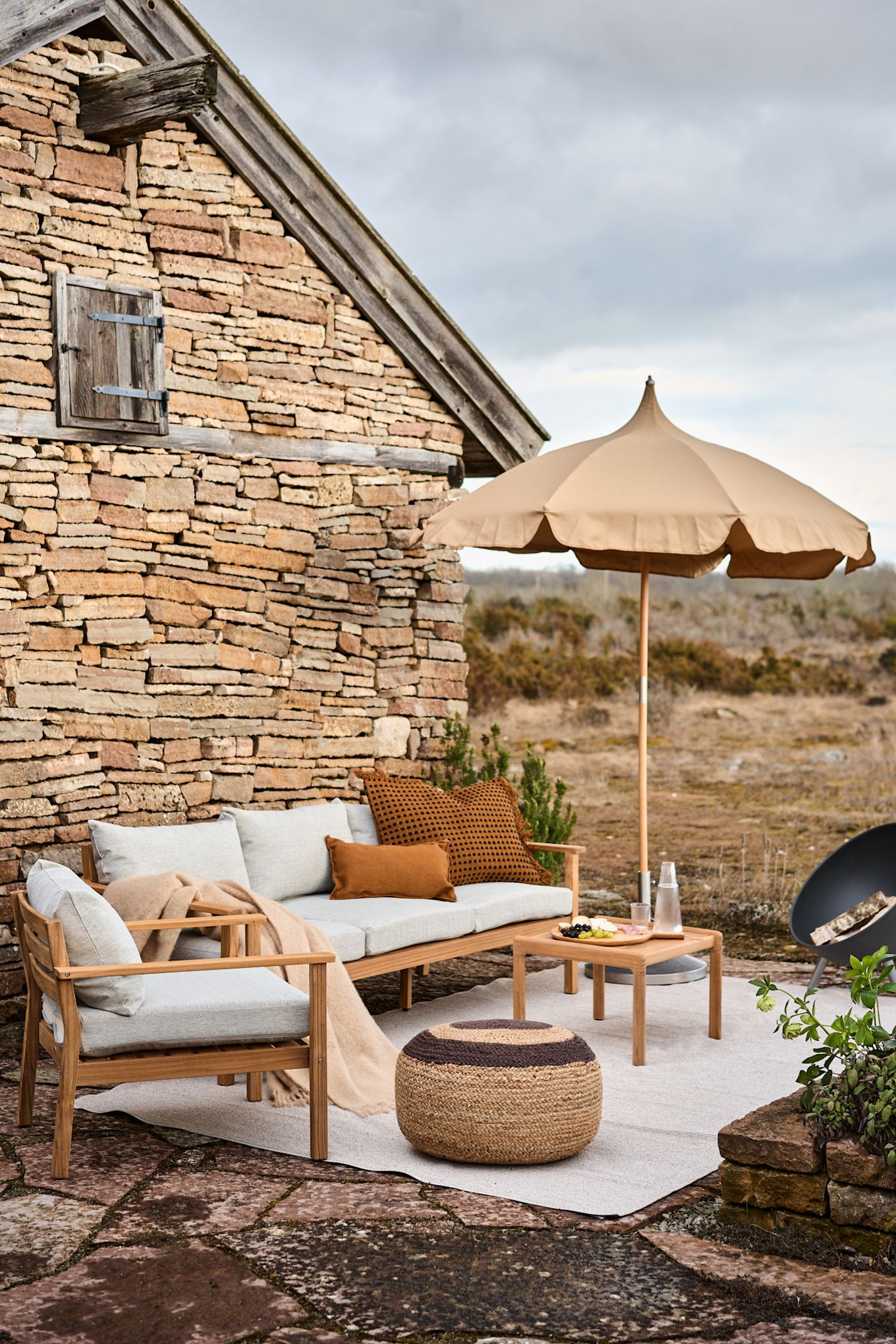 Een zithoek op een mediterraan terras met de beige Lull parasol van Ferm Living en het Melooni zitkussen van OYOY.