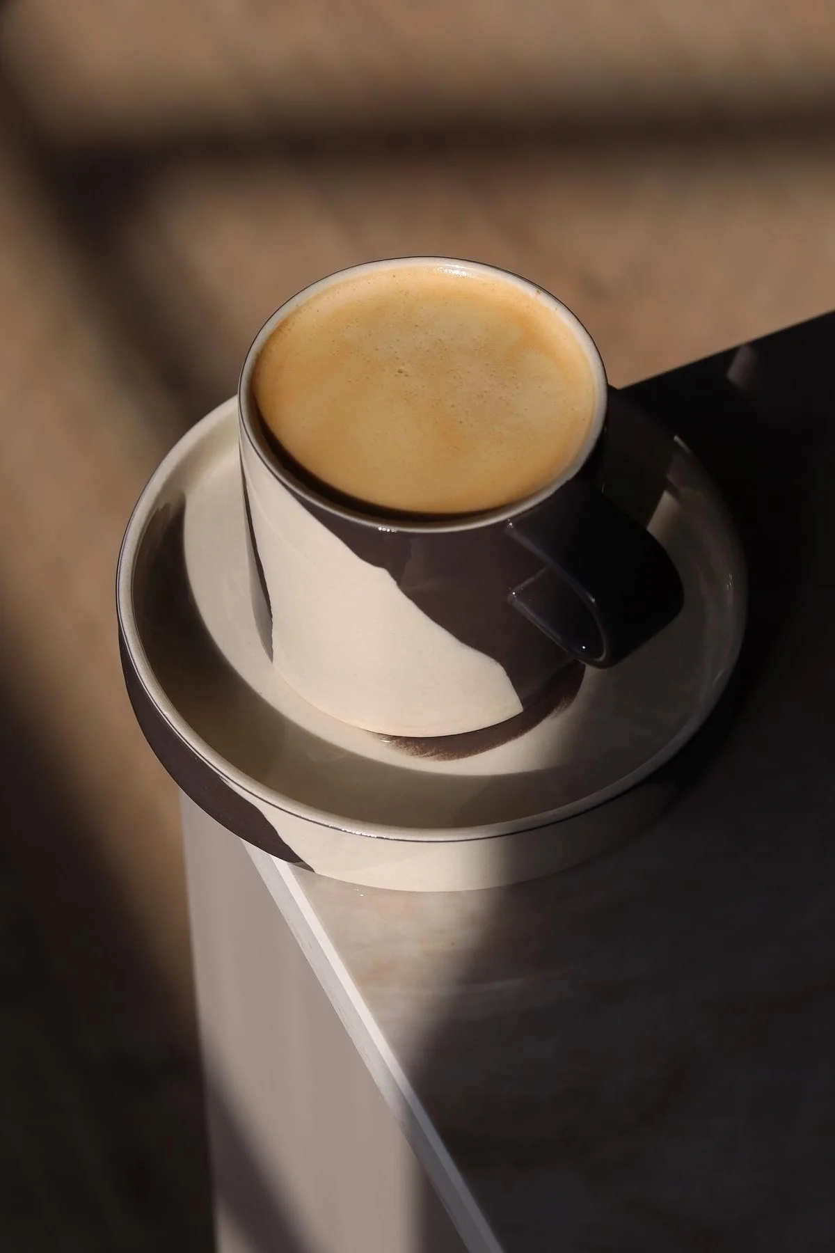 Koffiekopje en schotel met abstract bruin en crèmekleurig patroon, gevuld met koffie, op een tafel met schaduwen.