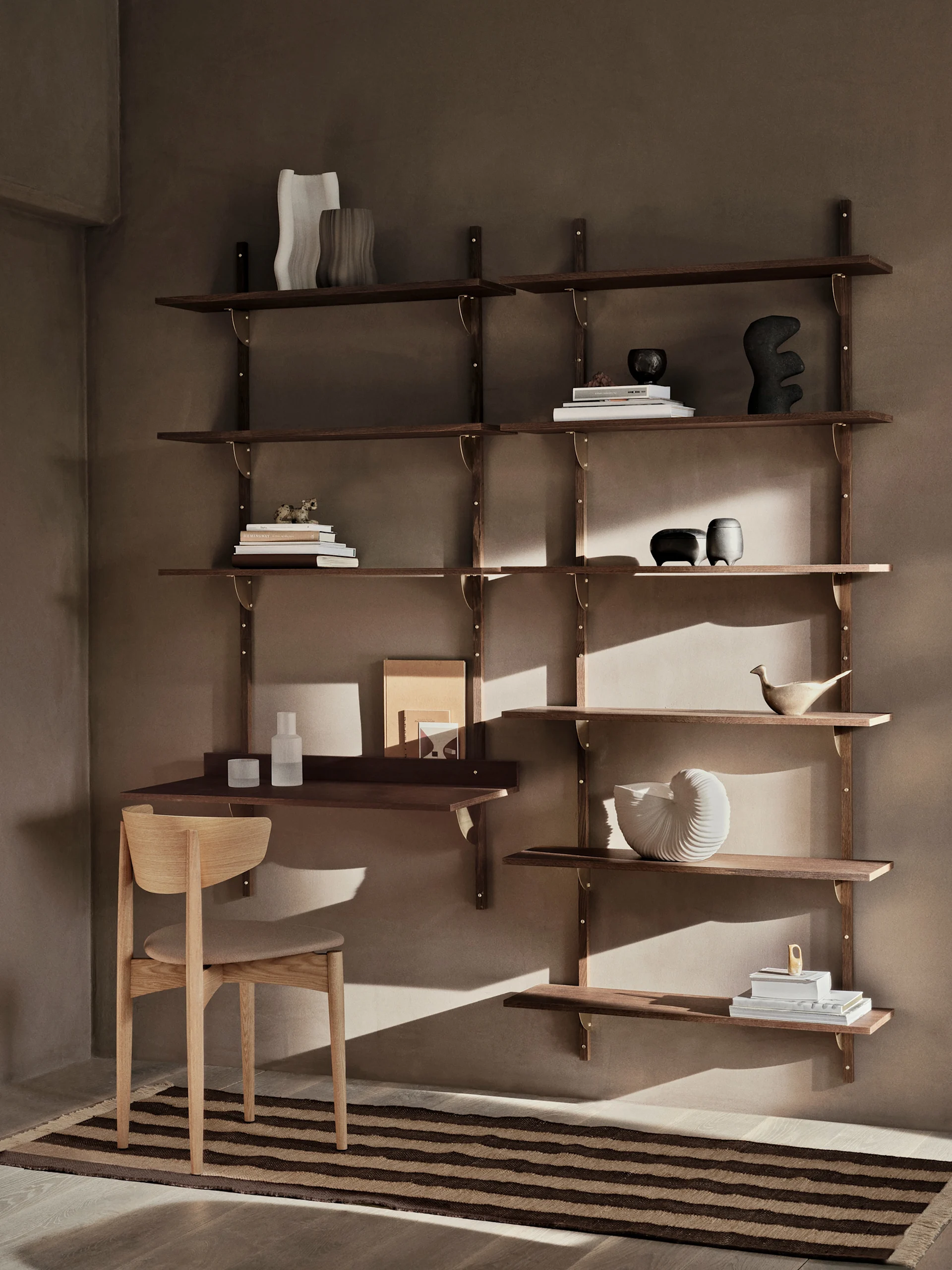 Een moderne donkerhouten wandkast met een bureau en stoel, versierd met boeken en decoratieve objecten, tegen een warme bruine muur met een gestreepte mat.