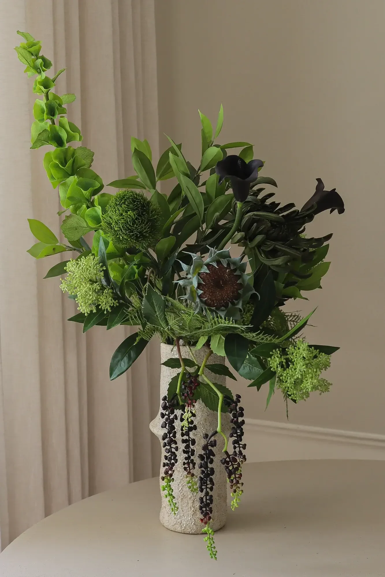 Een arrangement van groen blad, donkere aronskelken en hangende bessen in een gestructureerde vaas.