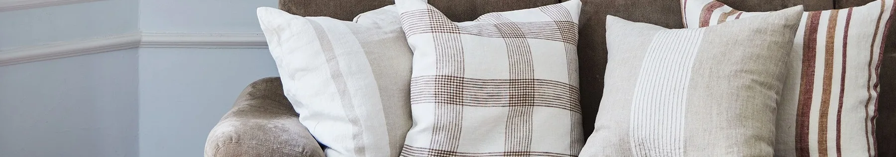 Close-up van drie kussens op een bruine bank, met witte, beige en geruite patronen met bruine en rode strepen.