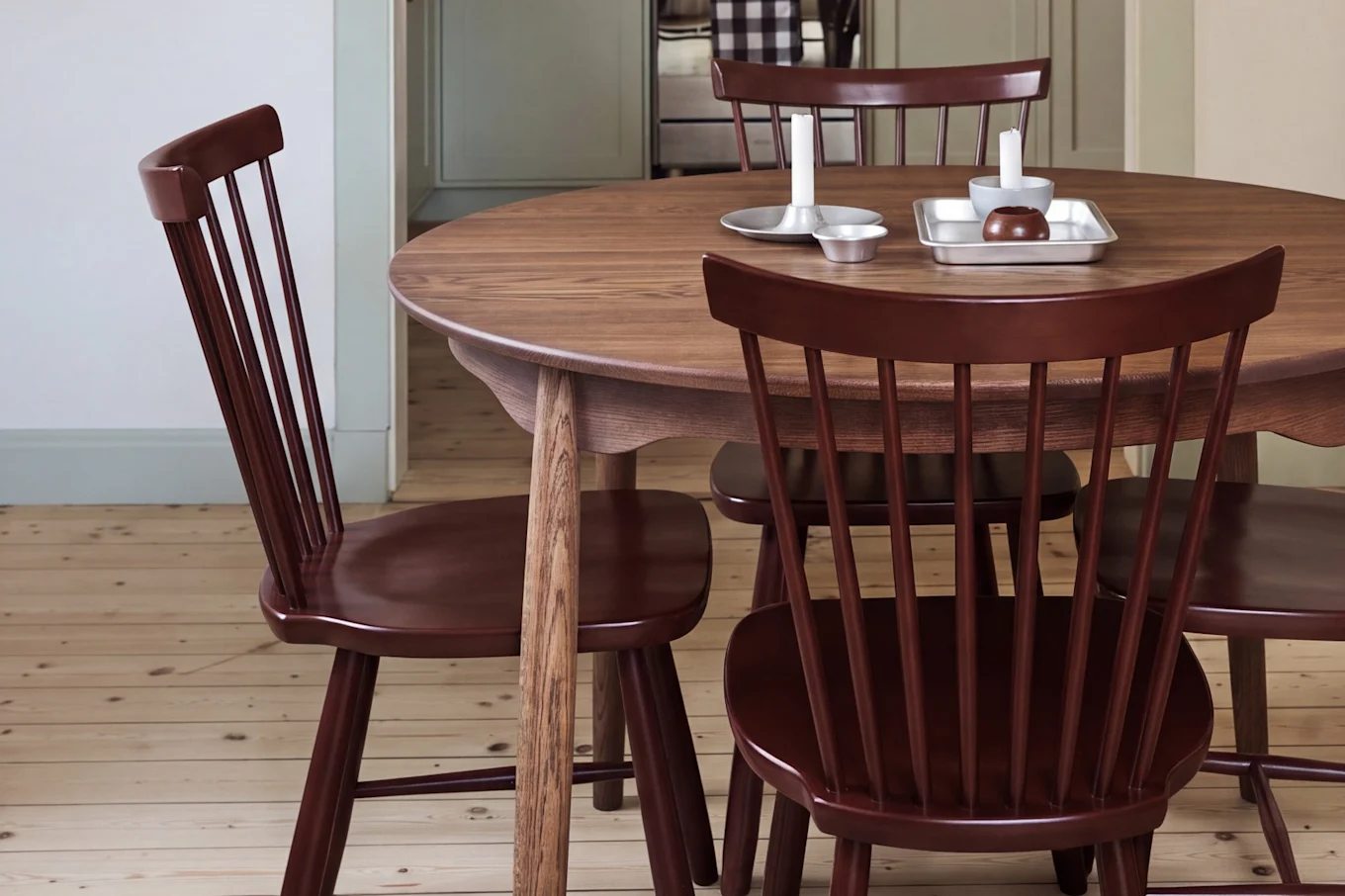 Eetkamer met ronde houten tafel, rode stoelen en een rode hanglamp, met uitzicht op een keuken met lichtgroene kasten.