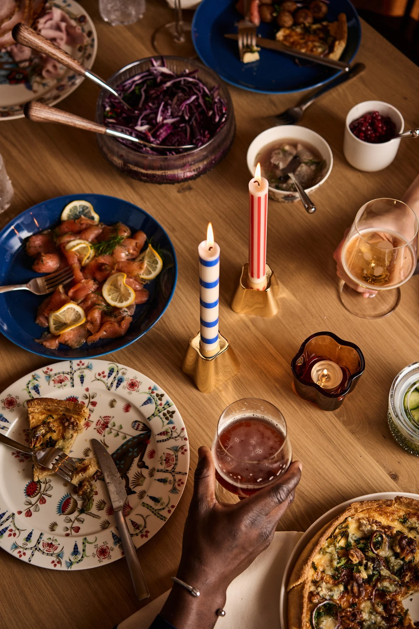 Een groep vrienden zit rond een sfeervol gedekte Zweedse kersttafel, versierd met kleurrijke gerechten en traditionele details. Ze heffen hun glazen, lachend en genietend van de feestelijke sfeer en elkaars gezelschap.