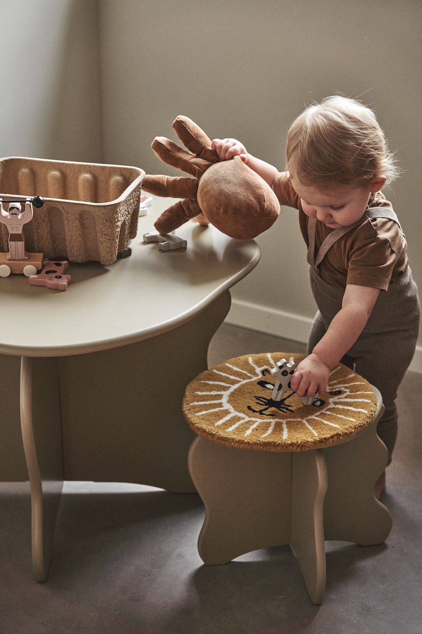 Een kleine tafel en stoelen zijn een must in een kinderkamer, hier zie je een klein kind met de Slope tafel en kruk van Ferm Living. 