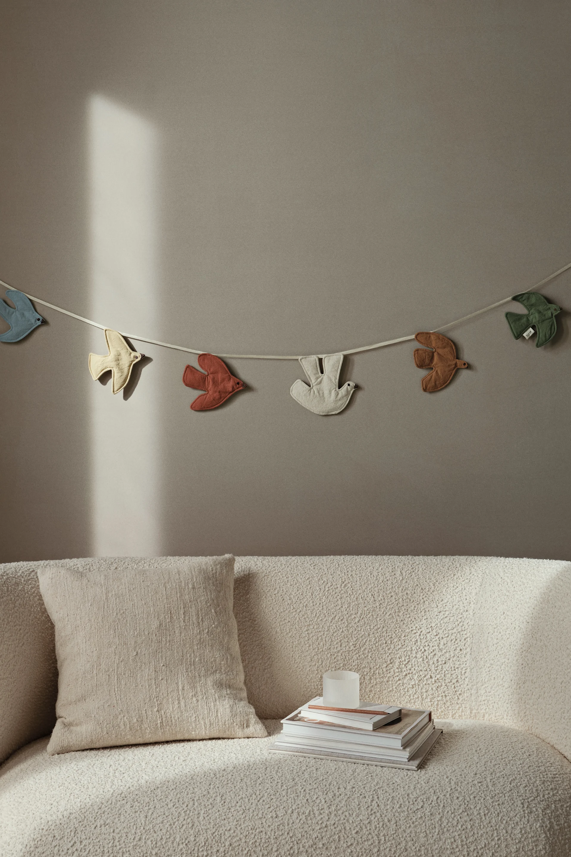 De Swif vogelslinger hangt aan een neutrale beige muur en brengt kleur en speelsheid in de kinderkamer. 