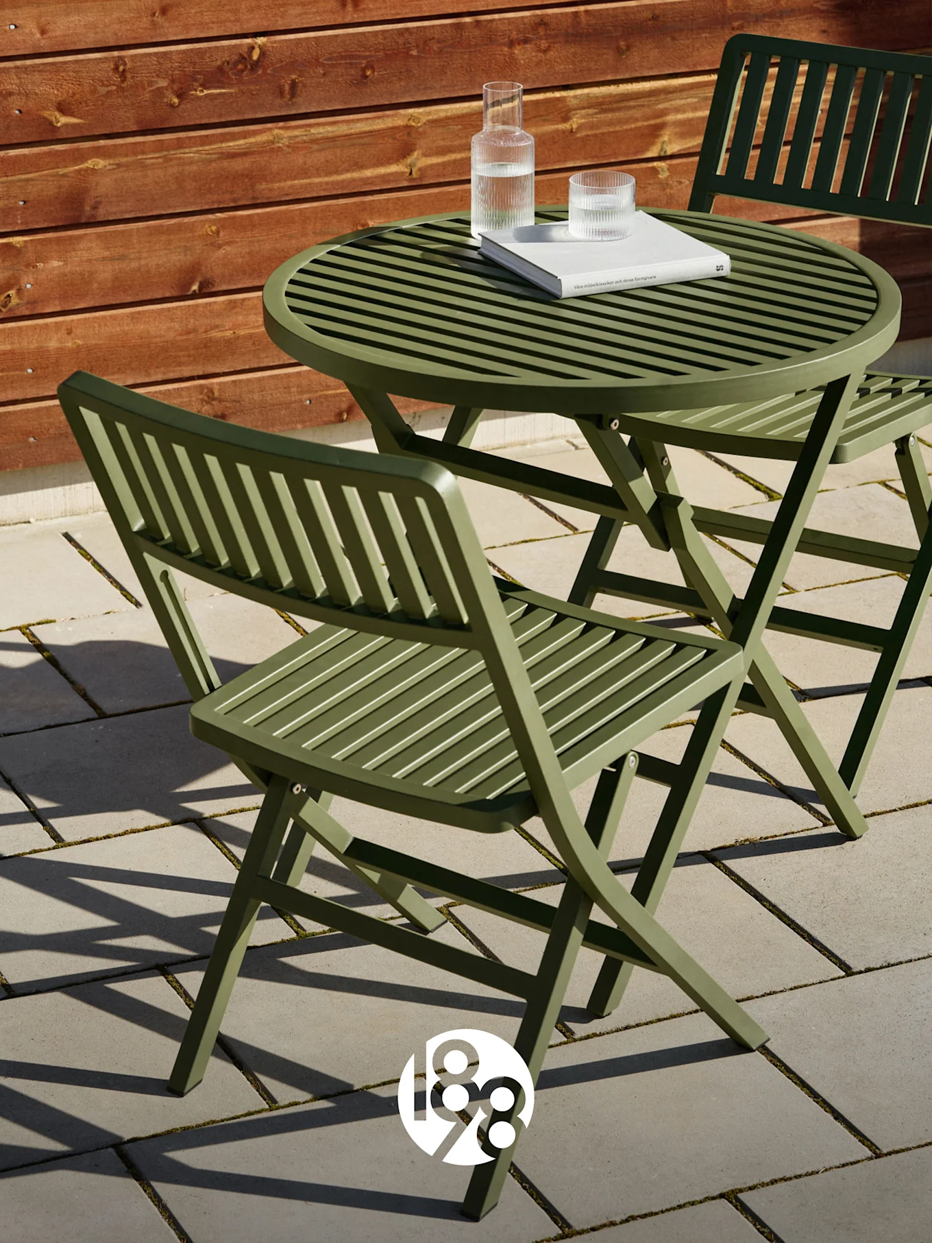 Twee groene latten inklapbare stoelen en een bijpassende tafel op een terras met een boek en waterglazen.