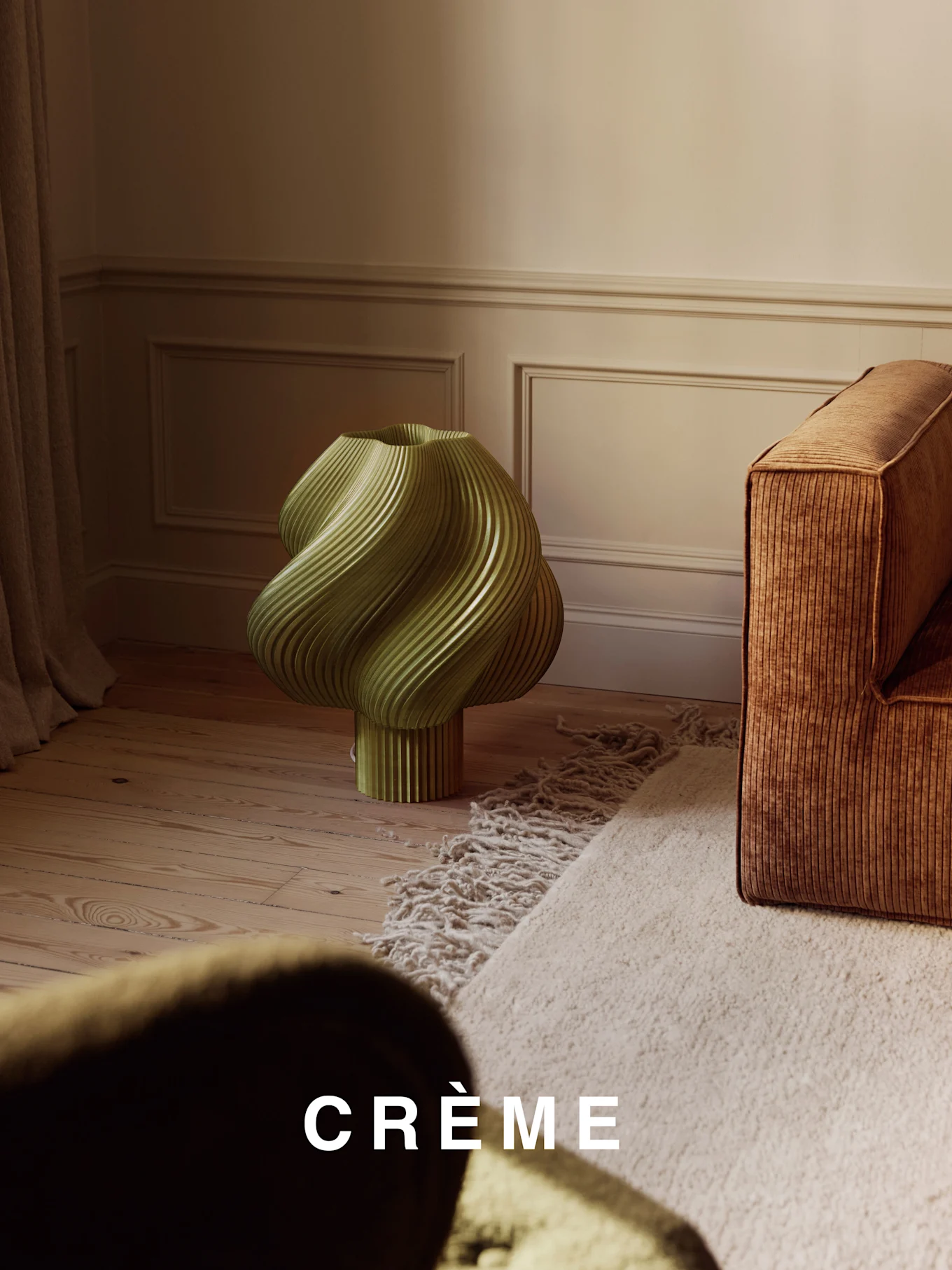 Een lichtgroene, gedraaide geribbelde lamp op een houten vloer, naast een bruine geribbelde bank en een beige shaggy tapijt.