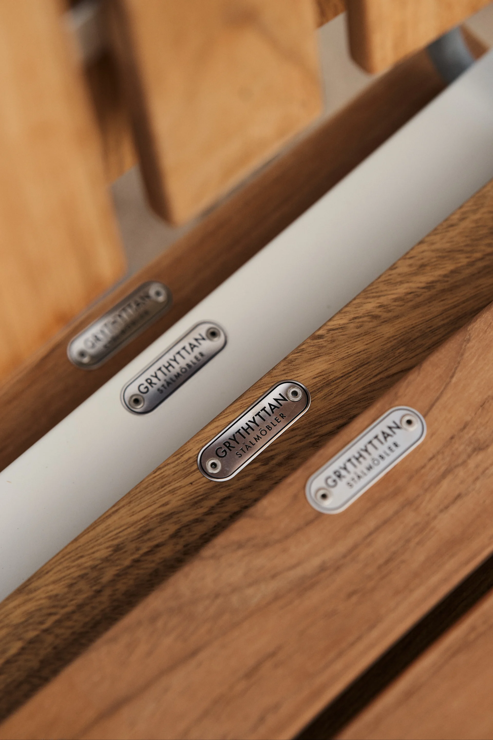 De A2-stoel van Grythyttan Stålmöbler is een icoon onder de buitenmeubelen in teak, hier een detailafbeelding van de zitting waar het logo in gegalvaniseerd staal als een mooi detail in zit.