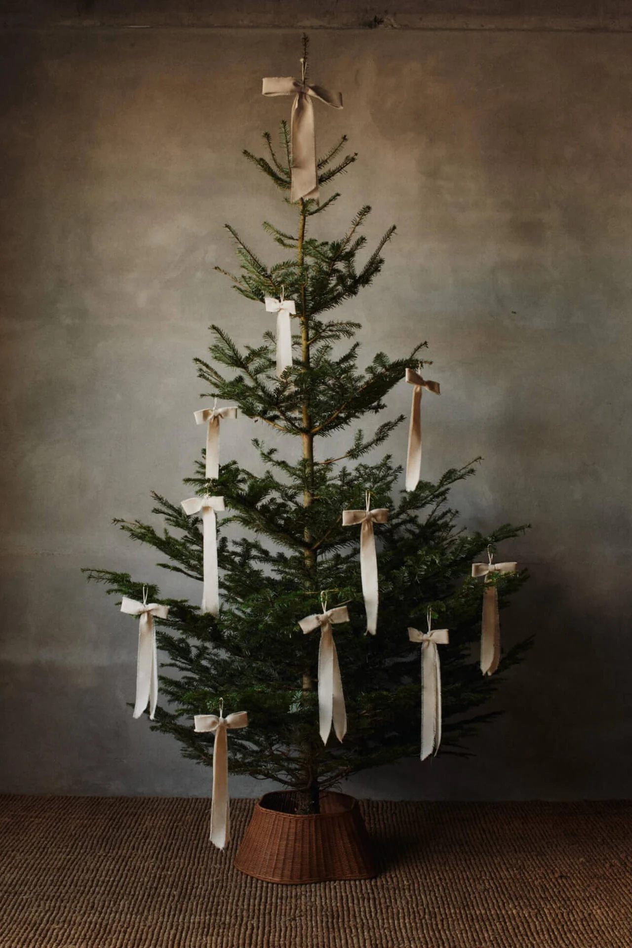 Vier witte brandende kaarsen, gerangschikt op een houten dienblad met een dennenappel en groenblijvende takken, op een houten tafel.