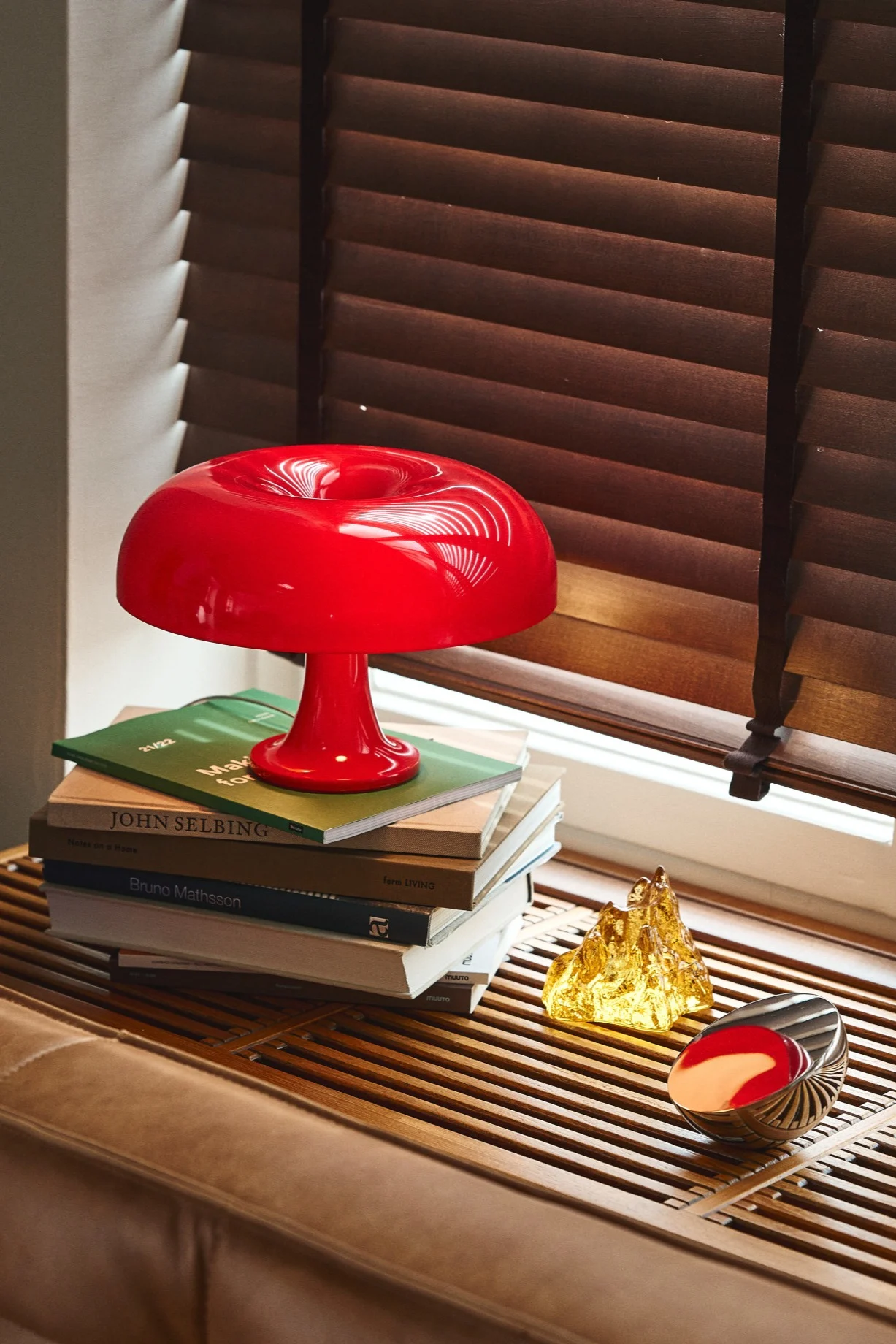 Update je huis met moderne lampen zoals de Instagram-favoriet Nessino in rood van Artemide. Hier op een houten vensterbank met een gele kandelaar van Kosta Boda. 