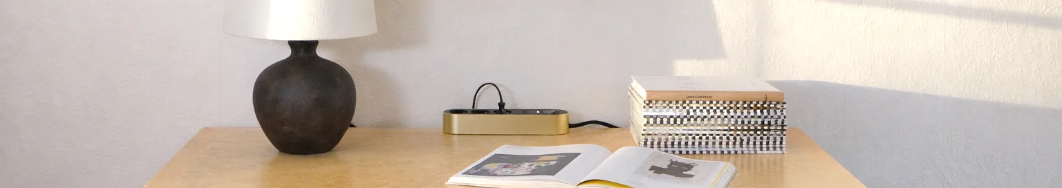 Gouden stekkerdoos met drie zwarte stopcontacten en een aan/uit-knop op een lichte ondergrond.