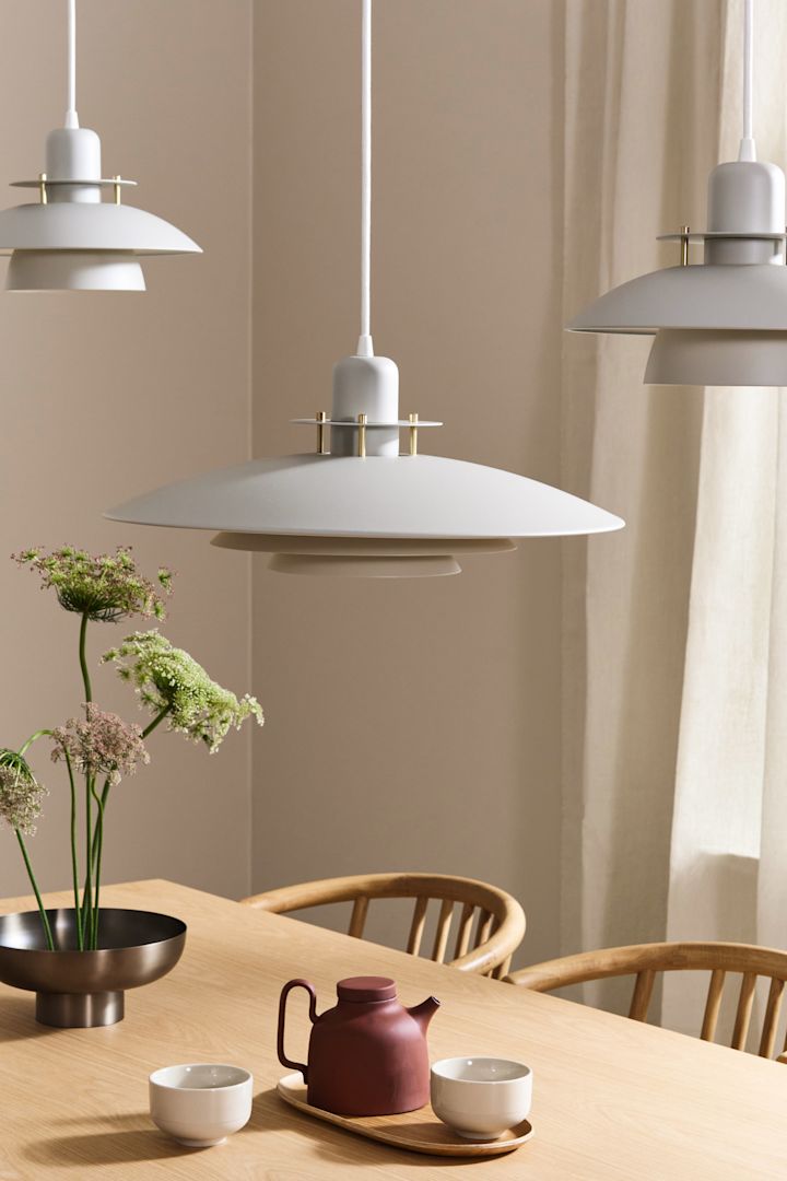 Drie witte Priums lampen van Belid hangen boven een eiken eettafel in Japandi-stijl. 