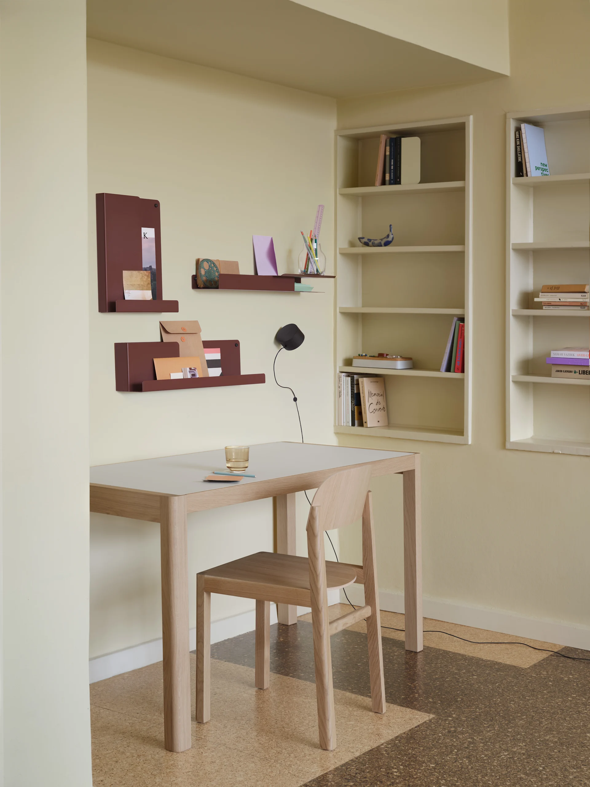 Een minimalistische kantoorinrichting met een licht houten bureau, stoel, roodbruine wandorganizers en ingebouwde boekenplanken.