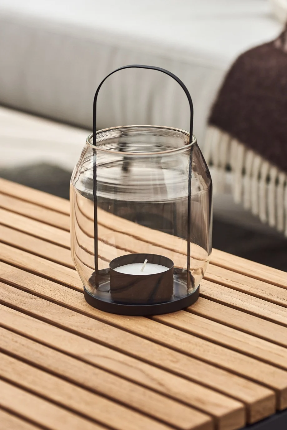 Lantaarns en windlichten voor buiten - hier zie je de ERNST lantaarn van glas en zwart metaal op een houten balkontafel staan.