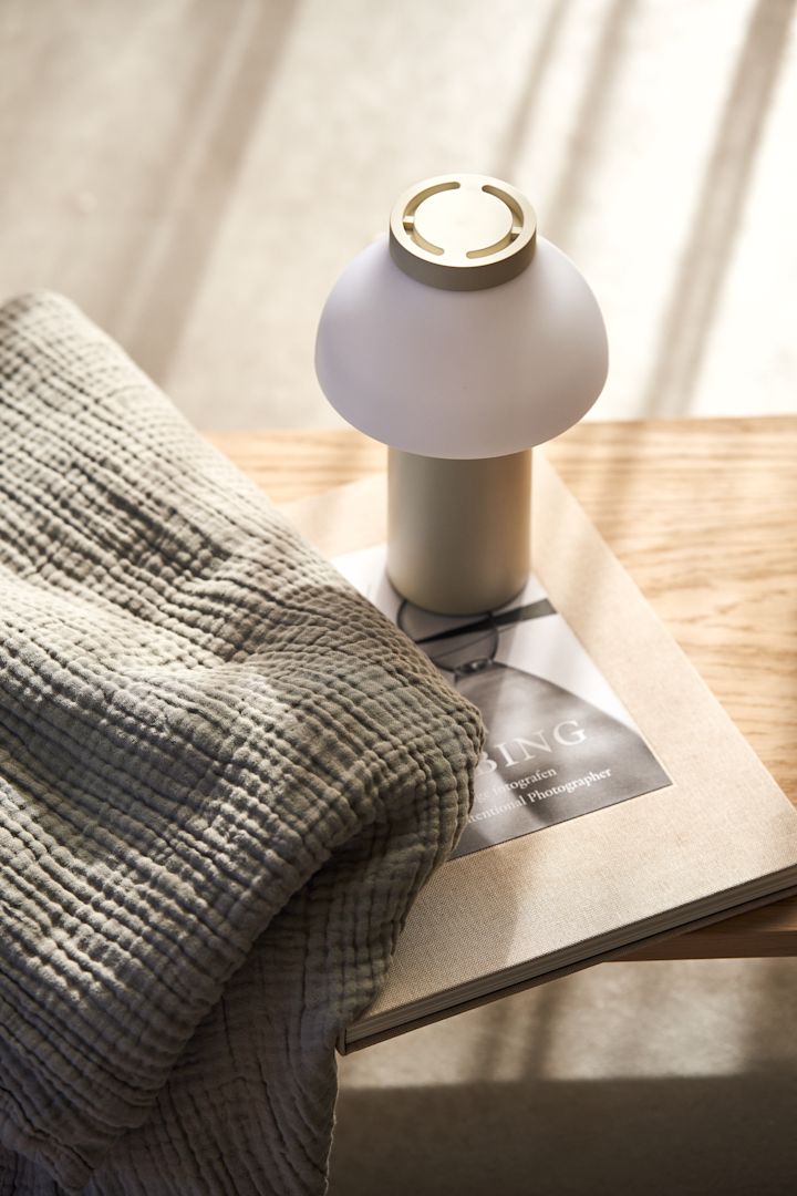 Ontdek trendy paddenstoellampen: Hier zie je de PC tafellamp van HAY op een tafel naast een grijze deken.