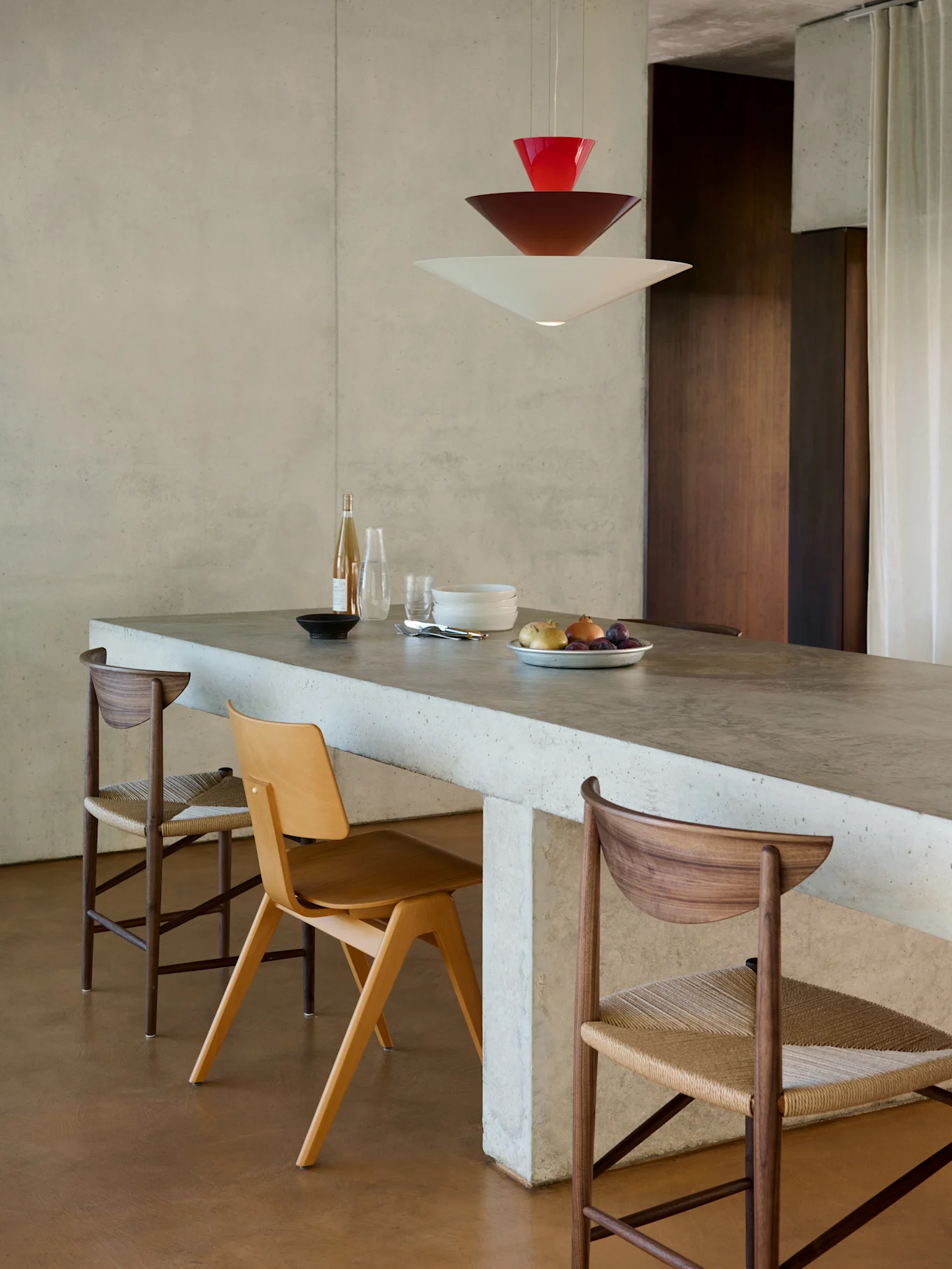 Moderne eethoek met betonnen eiland, drie stoelen en een gestapelde rode, bruine en witte hanglamp.