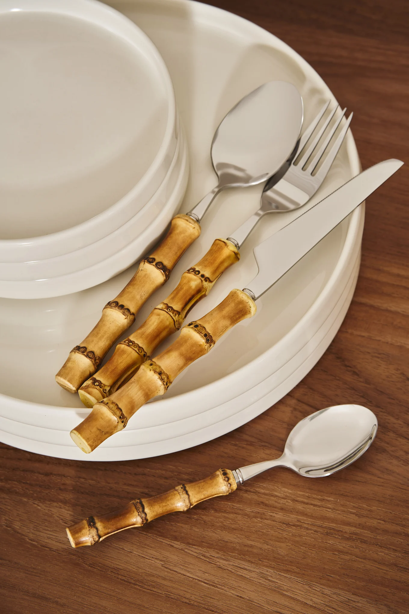 Bestek met bamboe handvatten op een stapel witte keramische borden en een houten tafel.