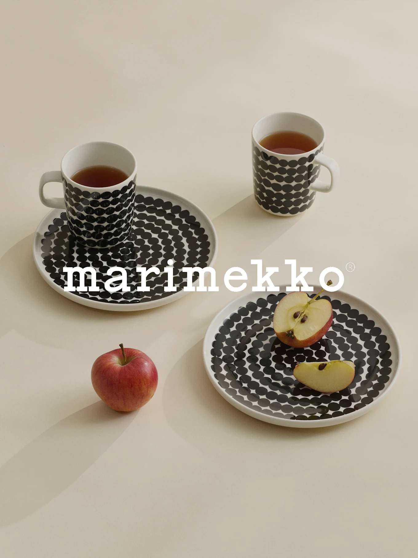 Twee mokken en borden met zwarte stippen, thee, rode appel, Marimekko-logo.